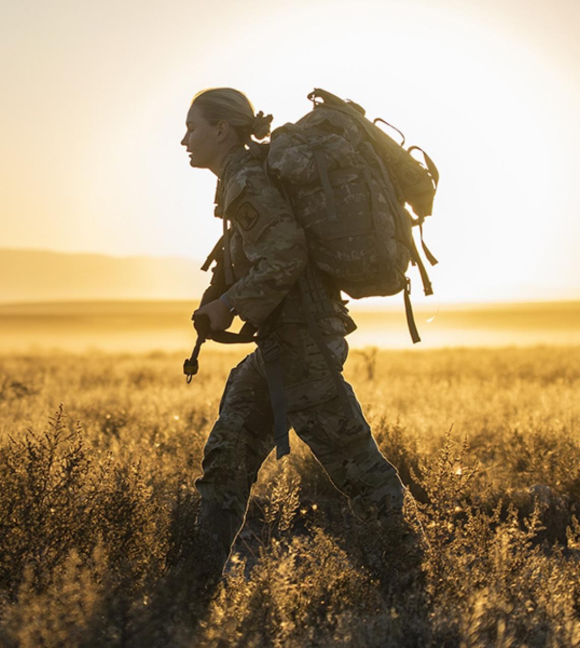 A soldier walking across a field during sunset.