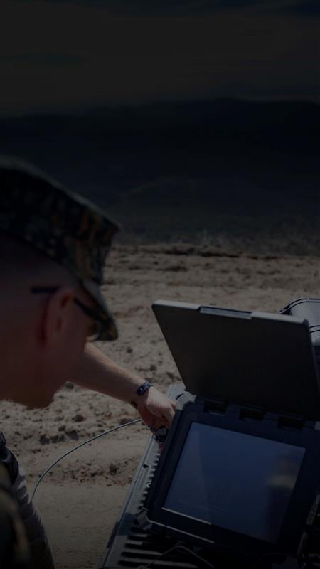 A man in military uniform stands confidently, holding a laptop computer in his hands, showcasing technology in service.