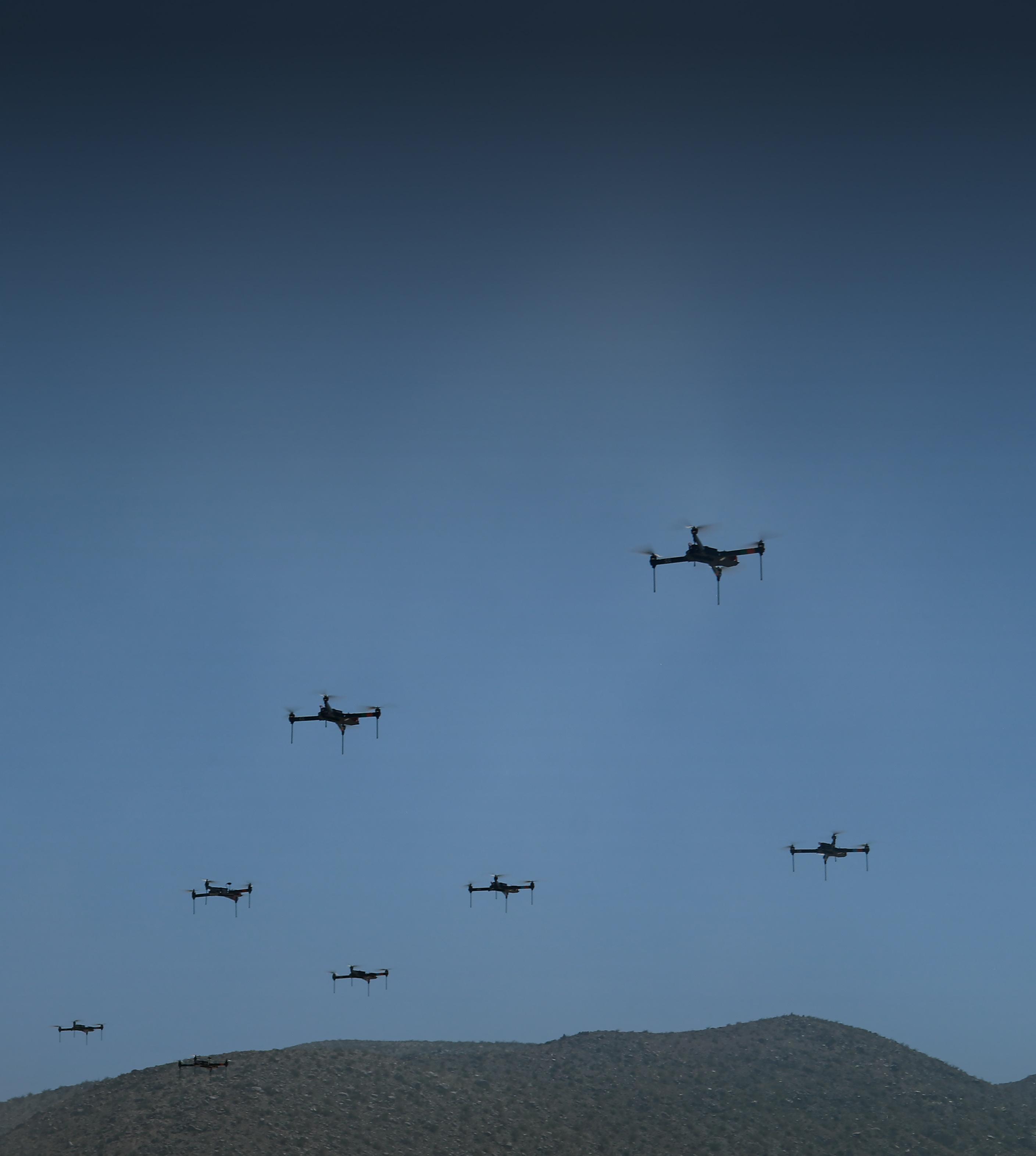 . A formation of drones flying over a vast desert landscape under a clear blue sky.