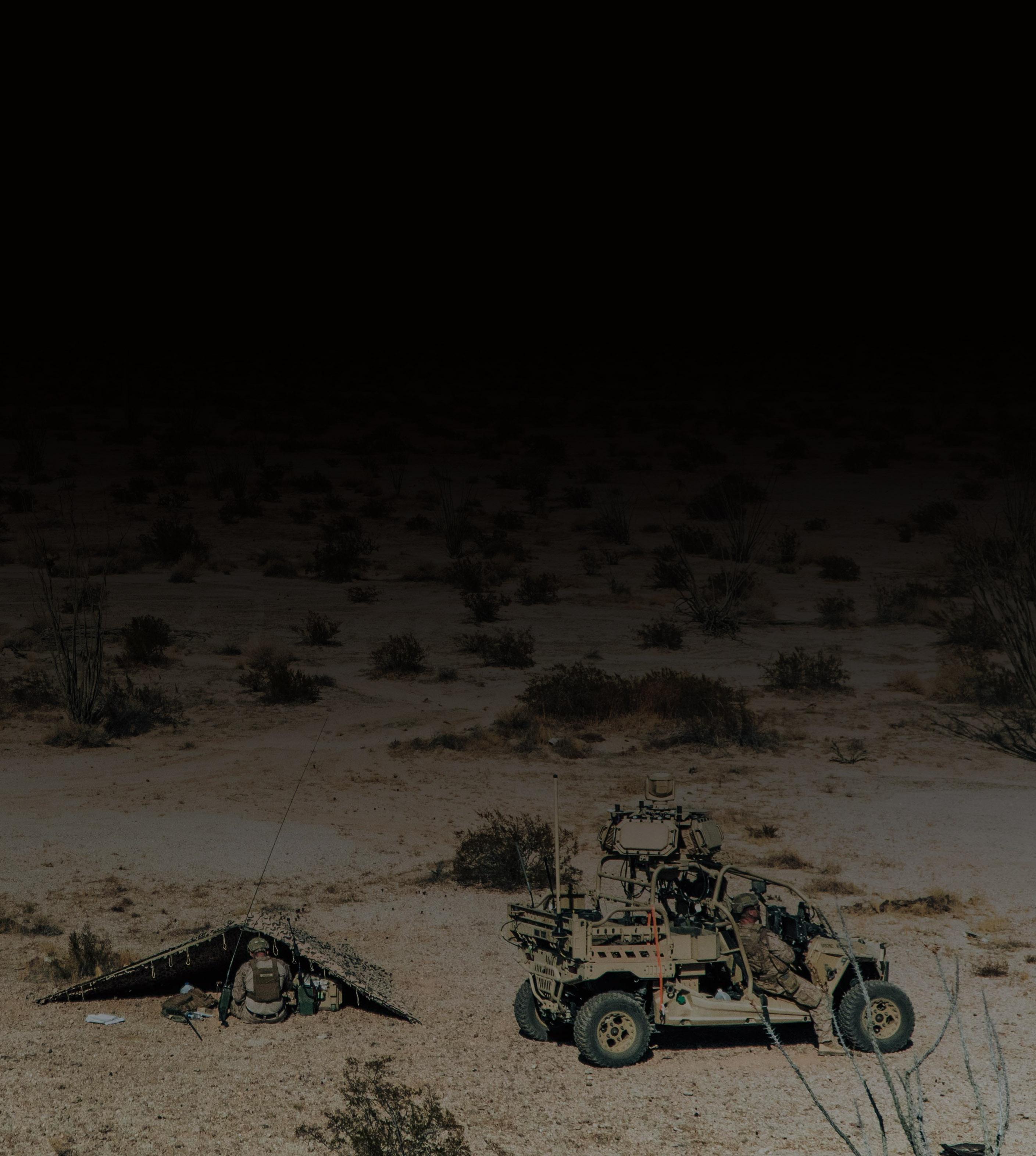A military vehicle parked on a sandy desert landscape under a clear blue sky.
