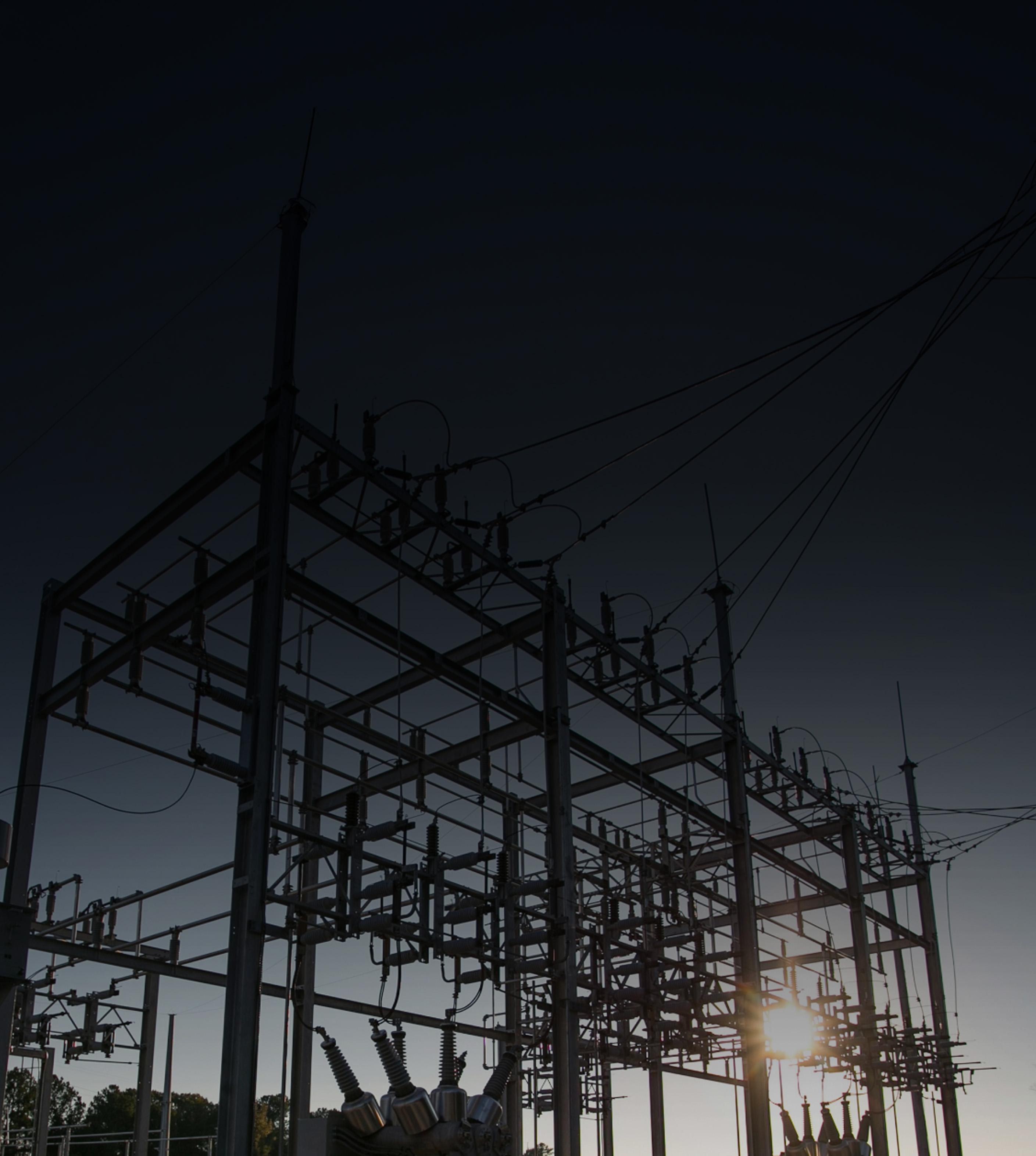 A large electrical substation featuring numerous wires and tall poles against a clear sky.