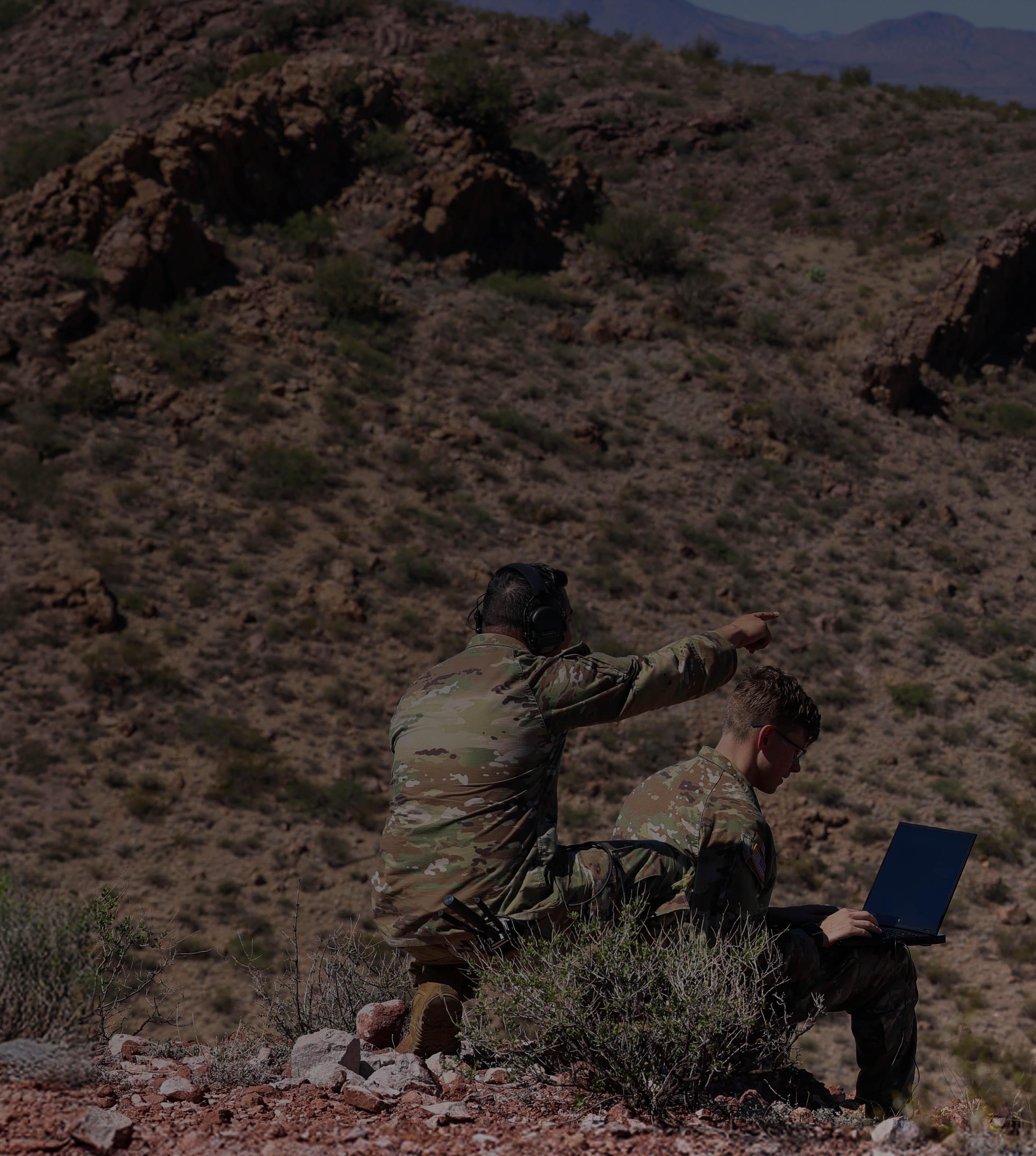 Two people sit on a grassy hillside, enjoying the view and each other's company under a clear blue sky.