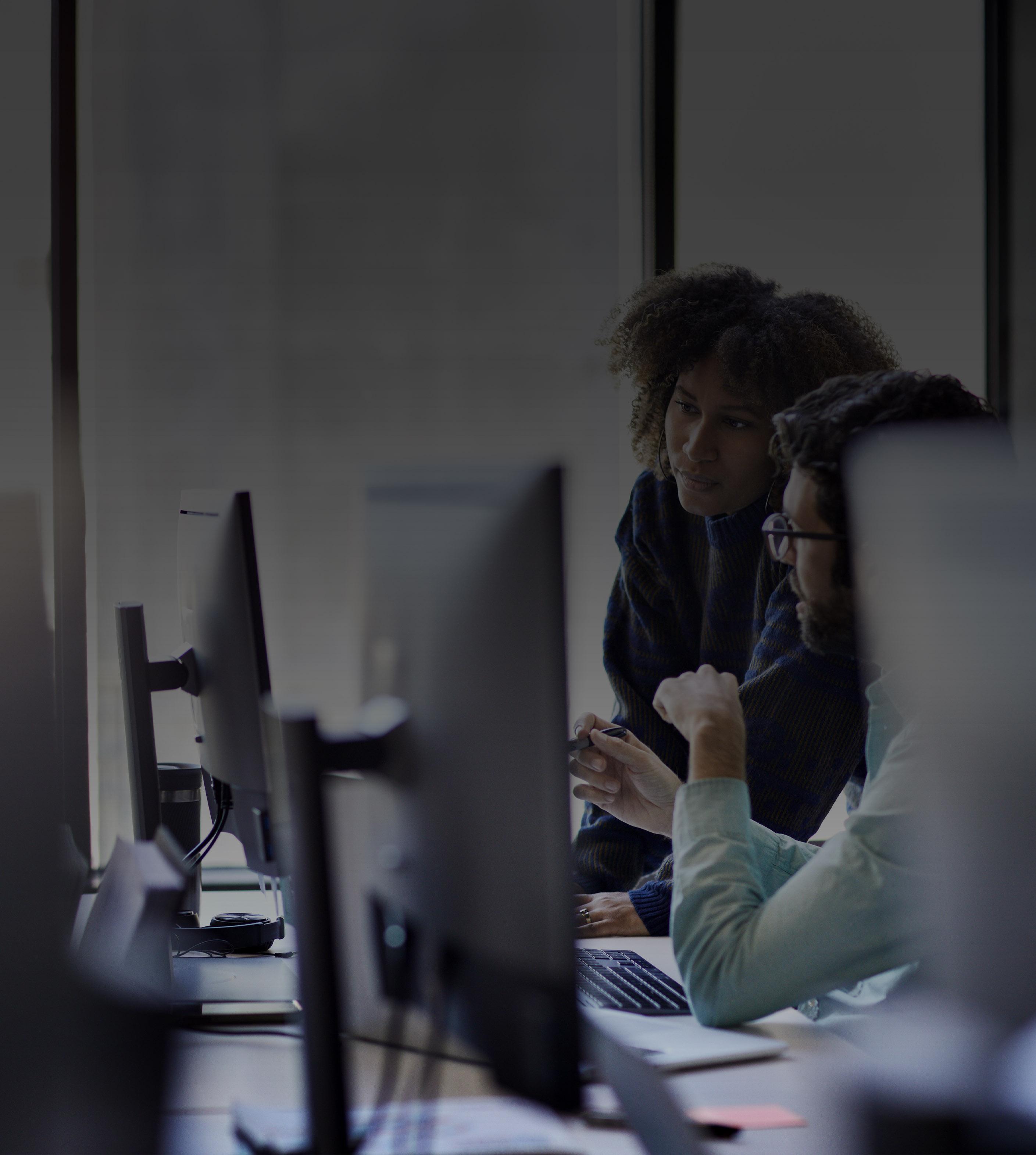Two individuals focused on their computers while collaborating in a modern office environment.