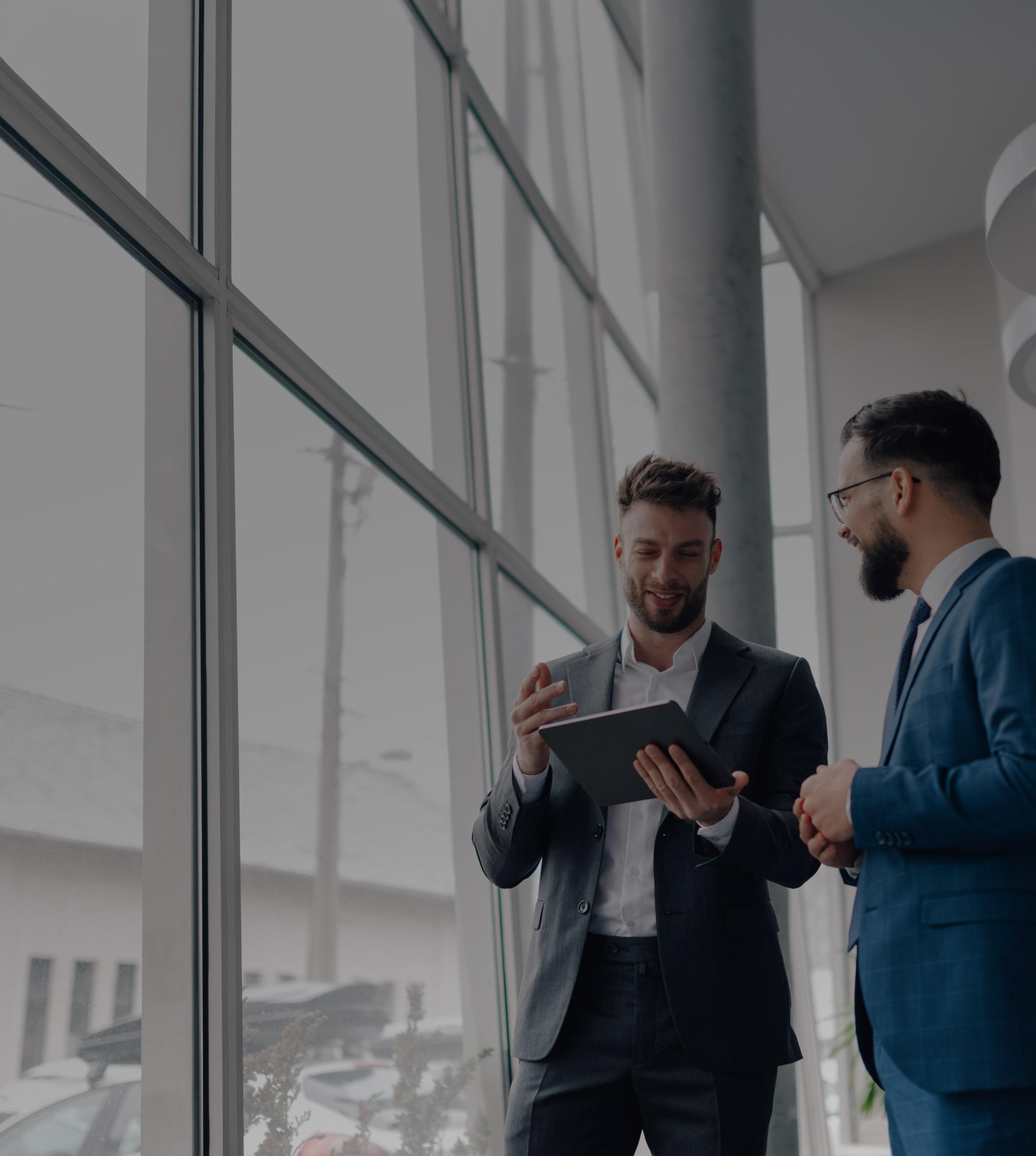 Two men in suits stand confidently in front of a modern building, engaged in conversation.