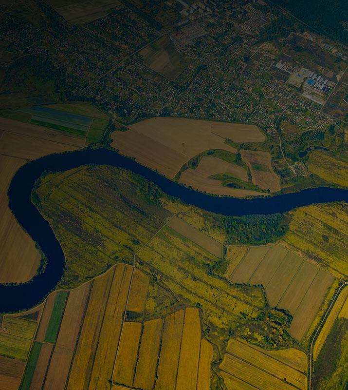 Aerial view showcasing a winding river surrounded by lush farmland and fields under a clear blue sky.