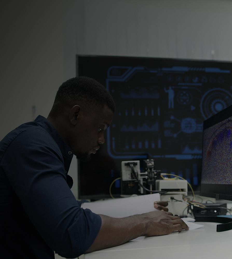A man seated at a desk, working on a laptop with a monitor beside him.