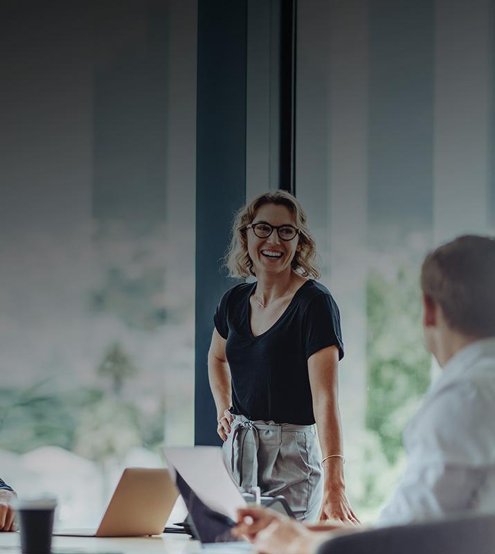 A woman speaks to a man in a meeting room, engaged in a professional discussion.