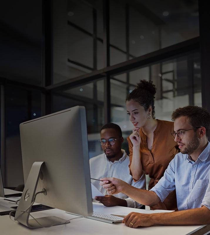 Three colleagues collaborating on a computer in a modern office setting.