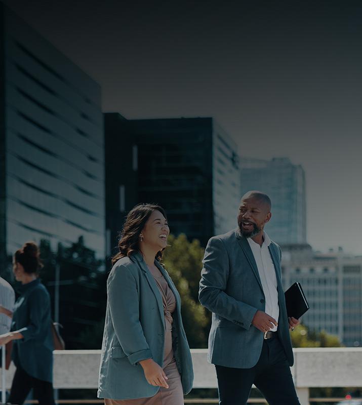 Three business professionals walking together on a city street, engaged in conversation and dressed in formal attire.