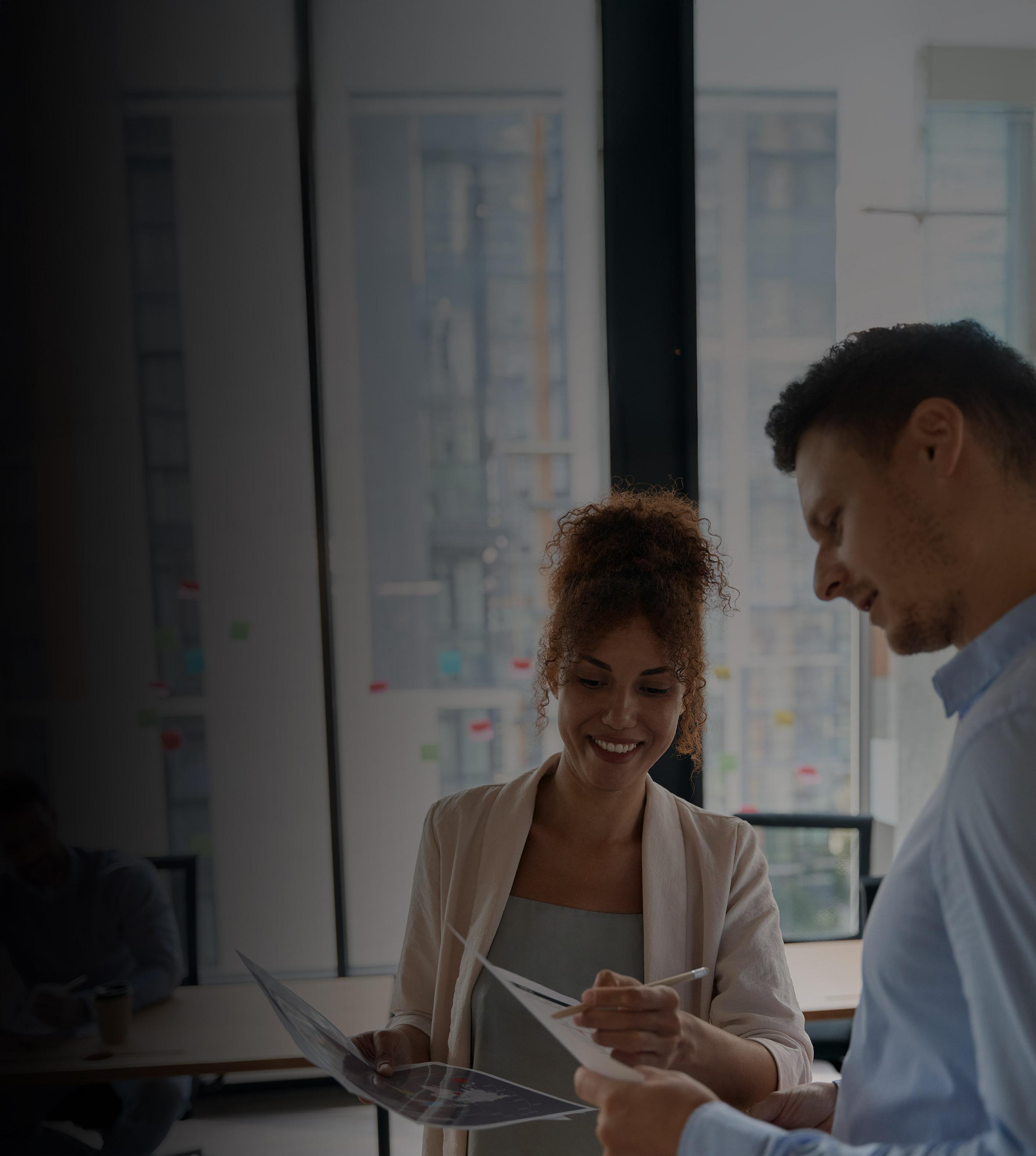 A man and woman review paperwork together in a modern office setting.