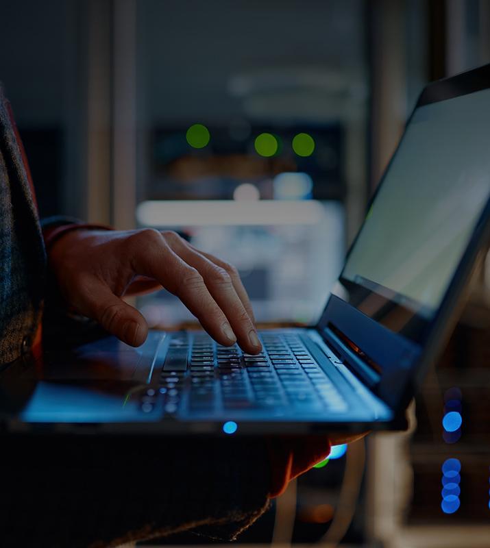 A person focused on typing on a laptop computer, with hands positioned on the keyboard and a screen illuminated.