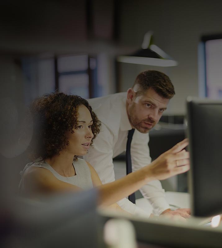 A man and woman collaborate on a computer in a modern office setting, focused on their work and sharing ideas.