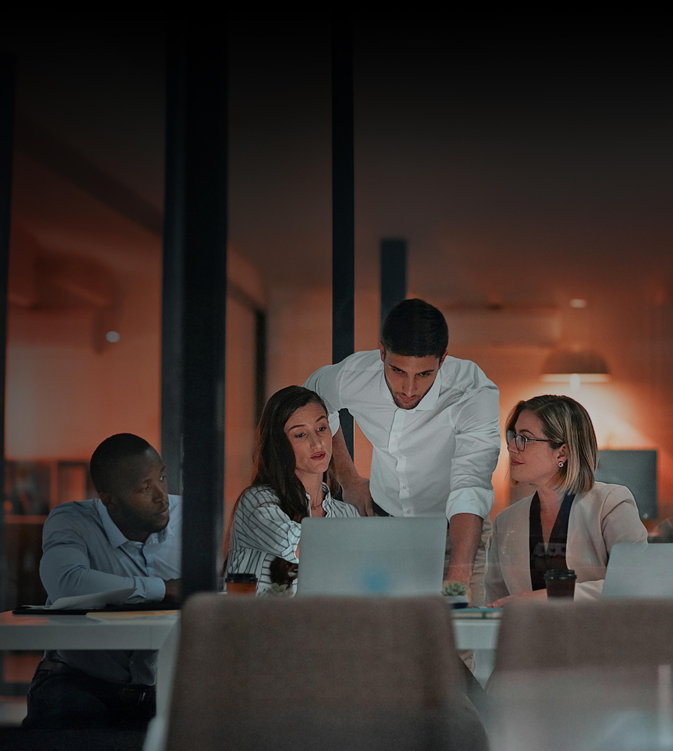 A group of diverse individuals seated at a table, each using laptops for collaborative work or discussion.
