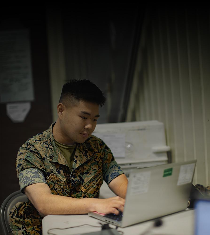 A man in military uniform seated at a desk, focused on paperwork in a professional office setting.