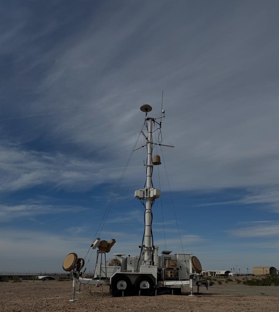 A tall metal tower with a satellite dish mounted at the top, set against a clear blue sky.