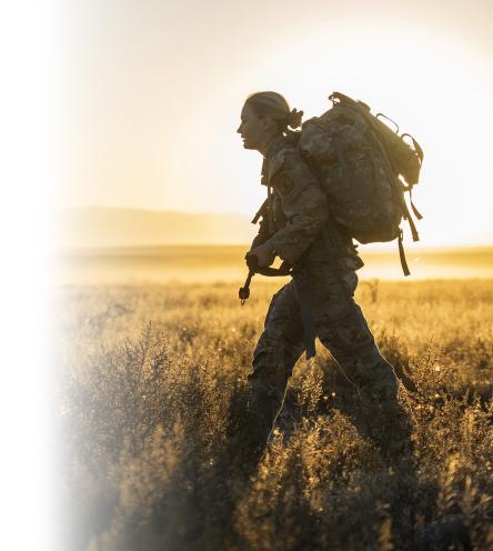 A soldier walking across a field during sunset.