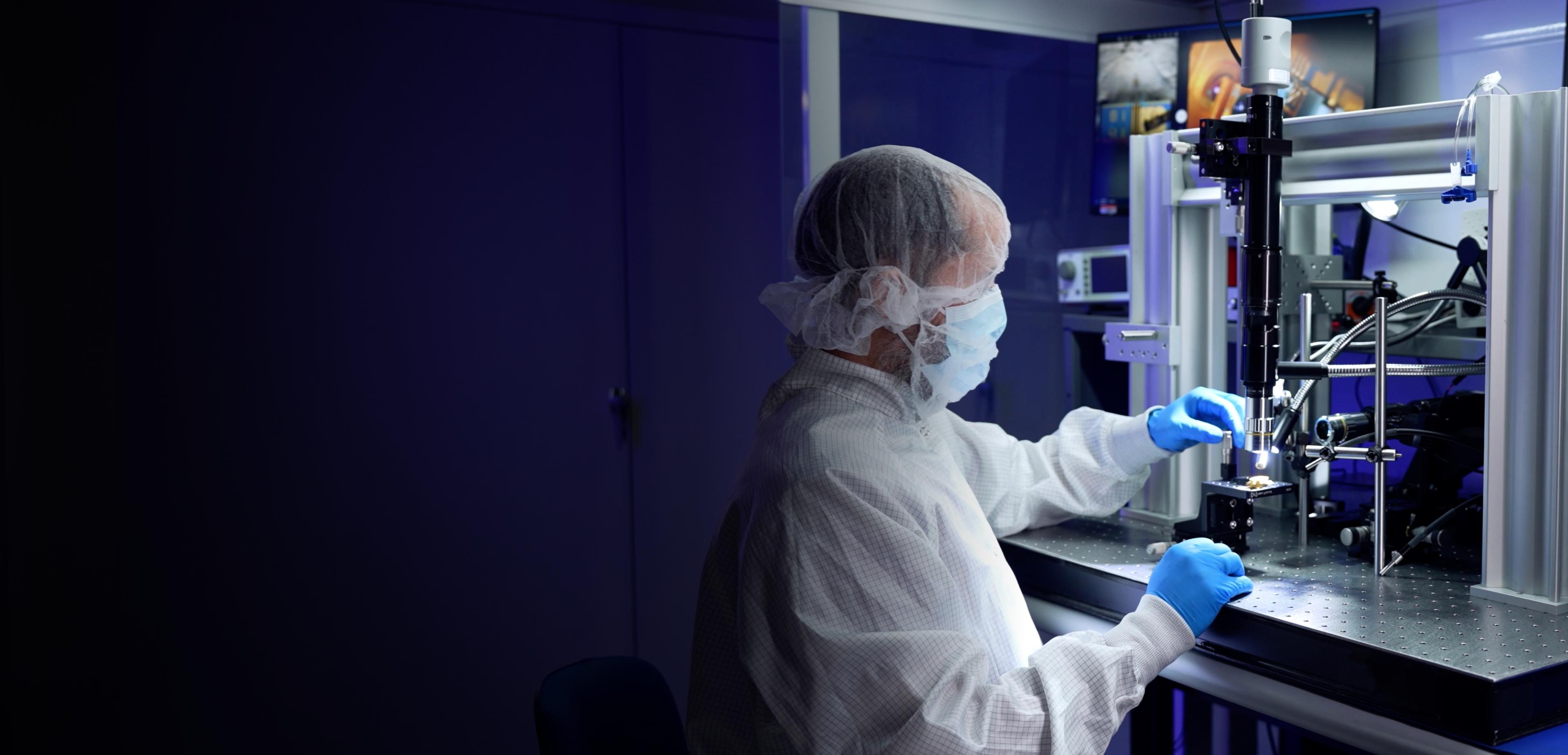 A person in a lab coat operates a complex machine, focused on their task in a laboratory setting.