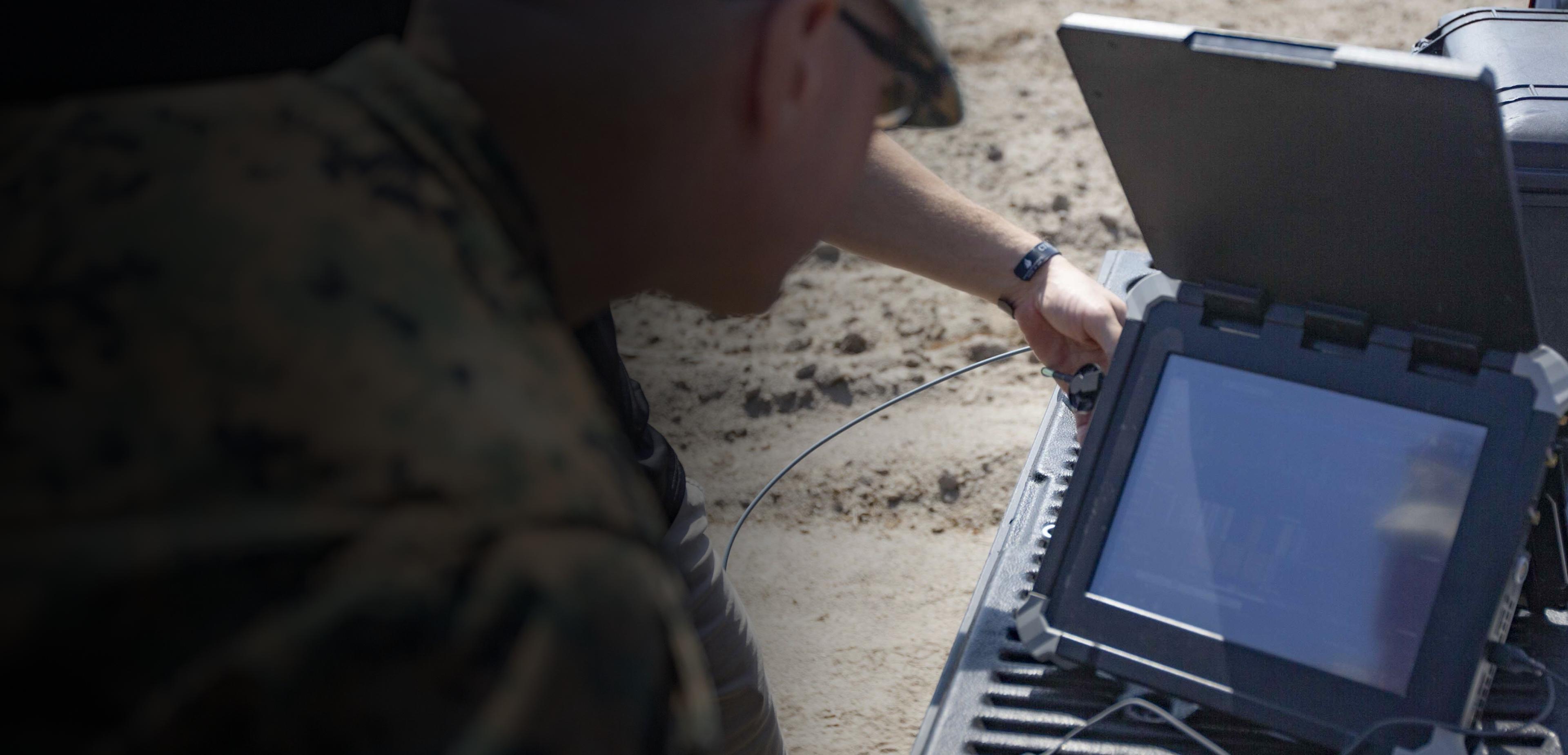 A man in military uniform stands confidently, holding a laptop computer in his hands, showcasing technology in service.