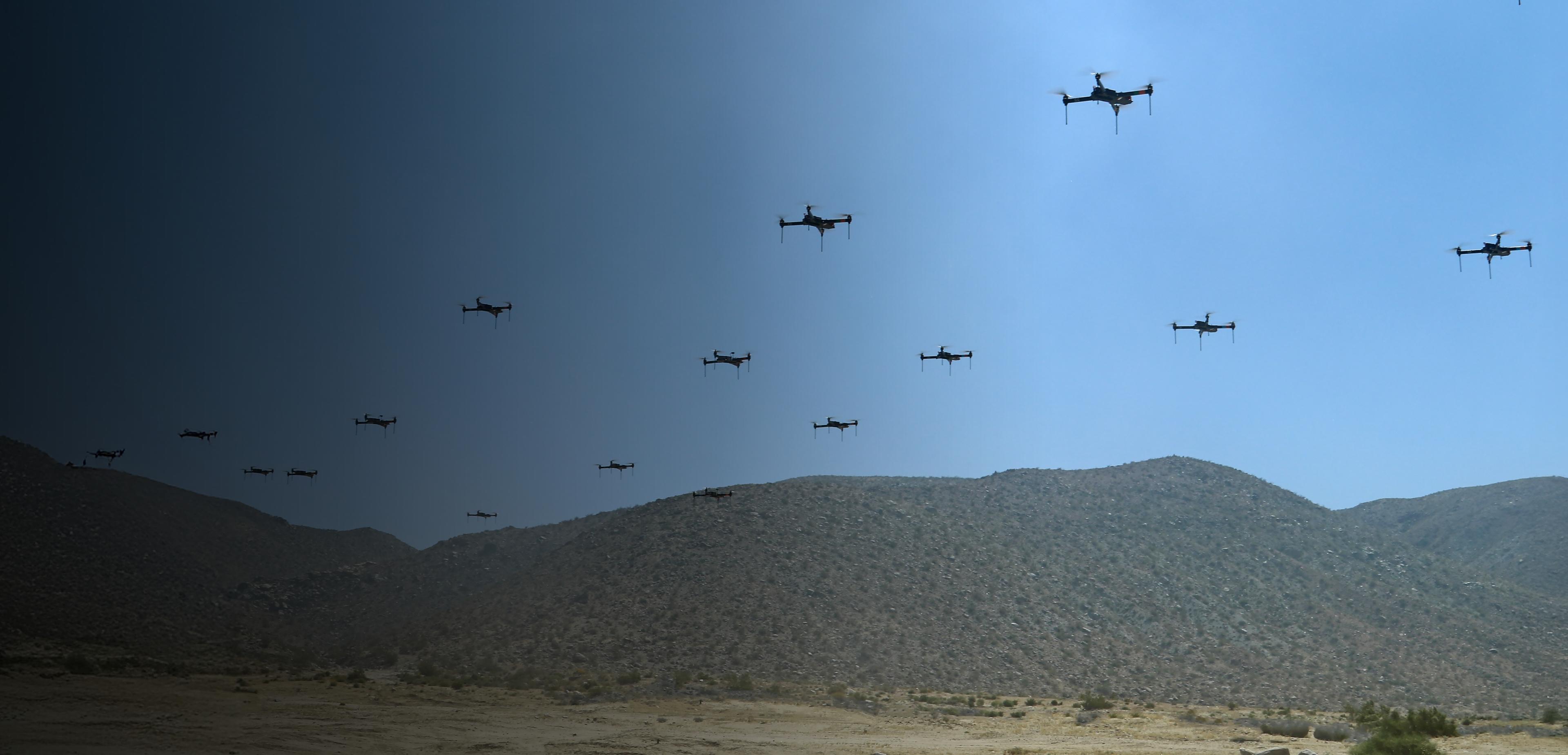 . A formation of drones flying over a vast desert landscape under a clear blue sky.