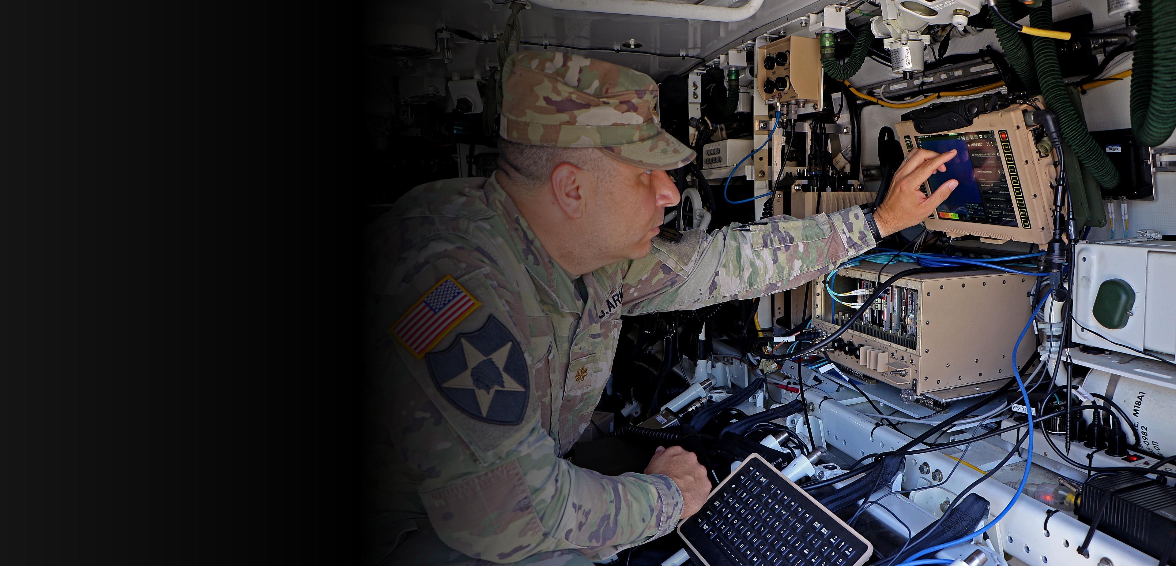 A soldier focused on a laptop computer, engaged in work while in a military setting.