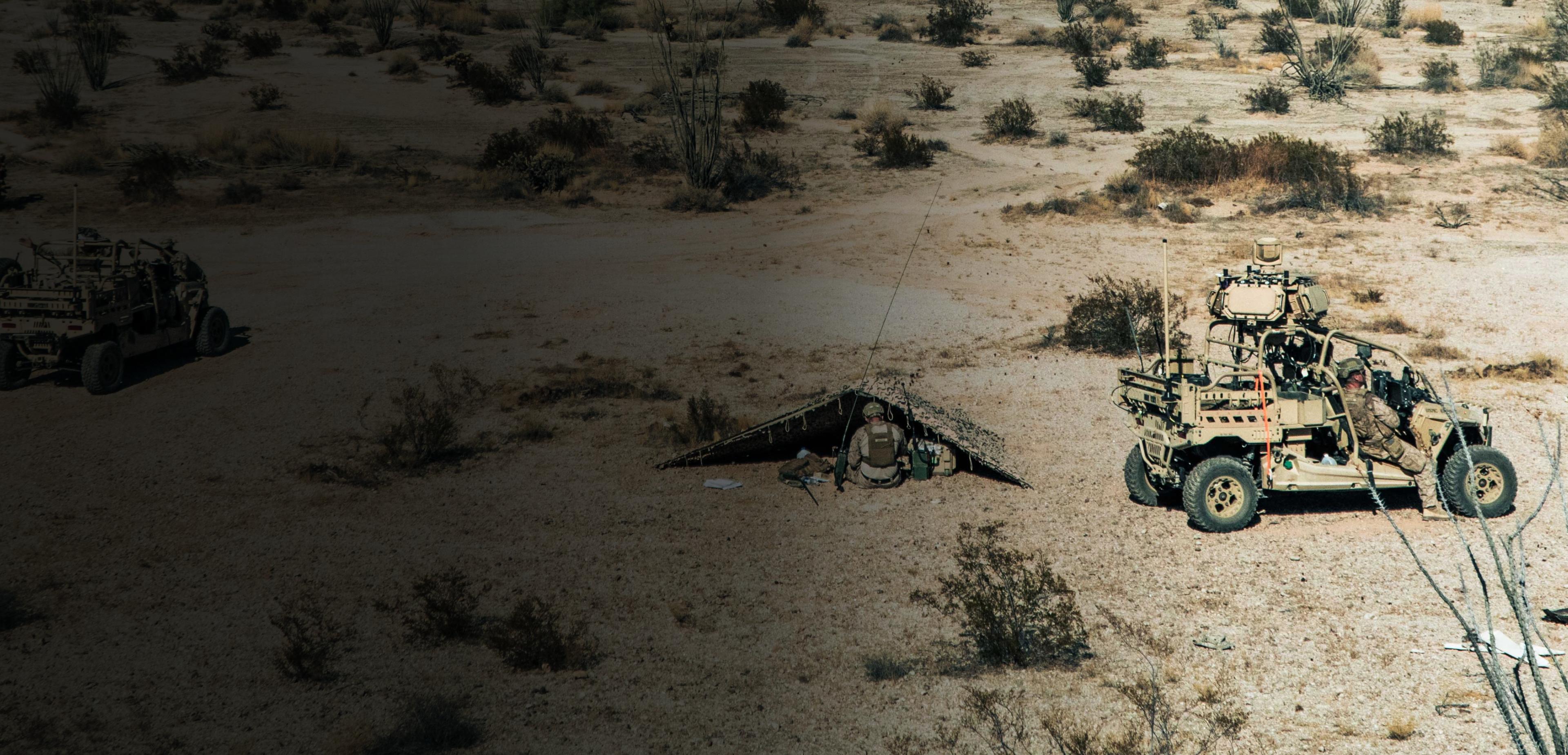 A military vehicle parked on a sandy desert landscape under a clear blue sky.
