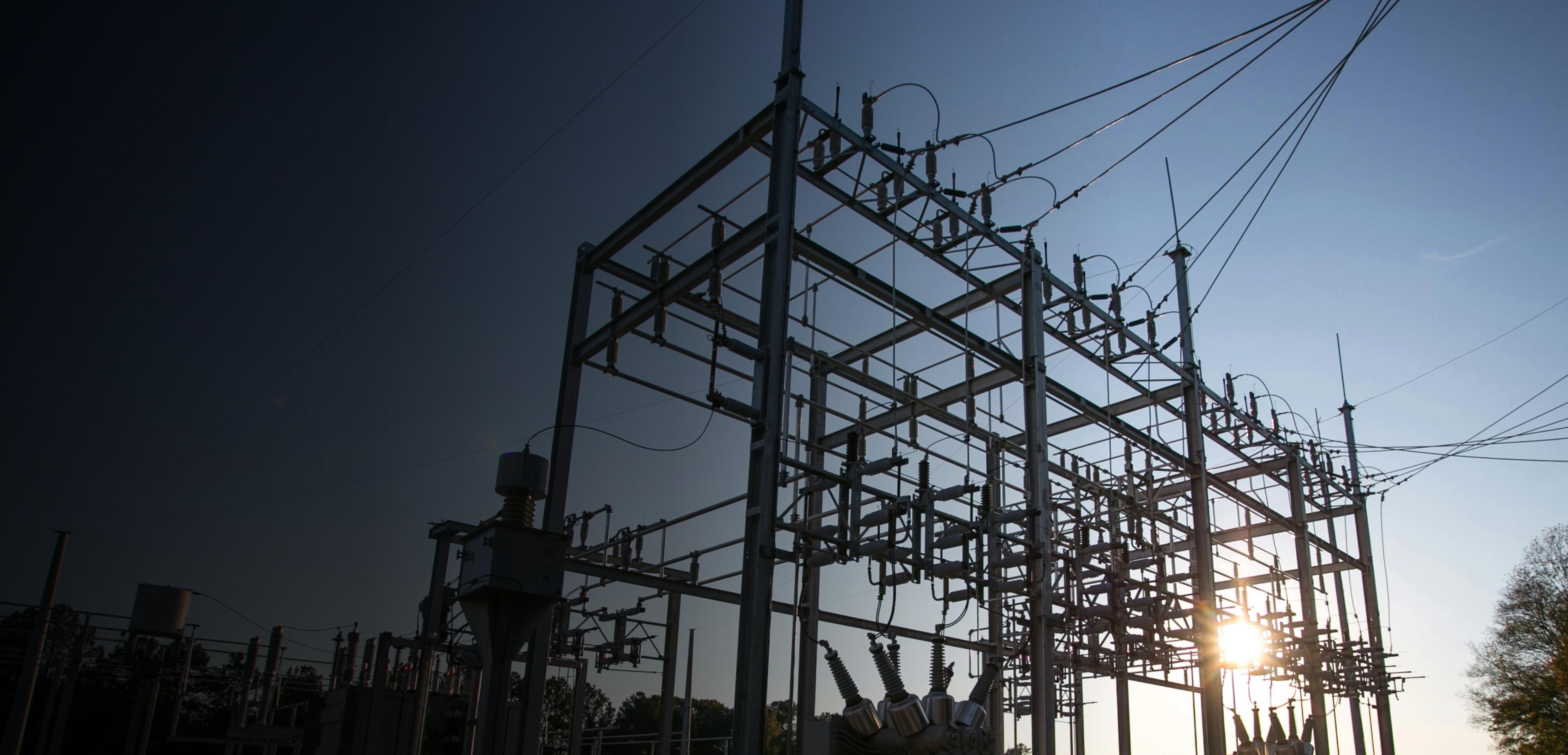 A large electrical substation featuring numerous wires and tall poles against a clear sky.
