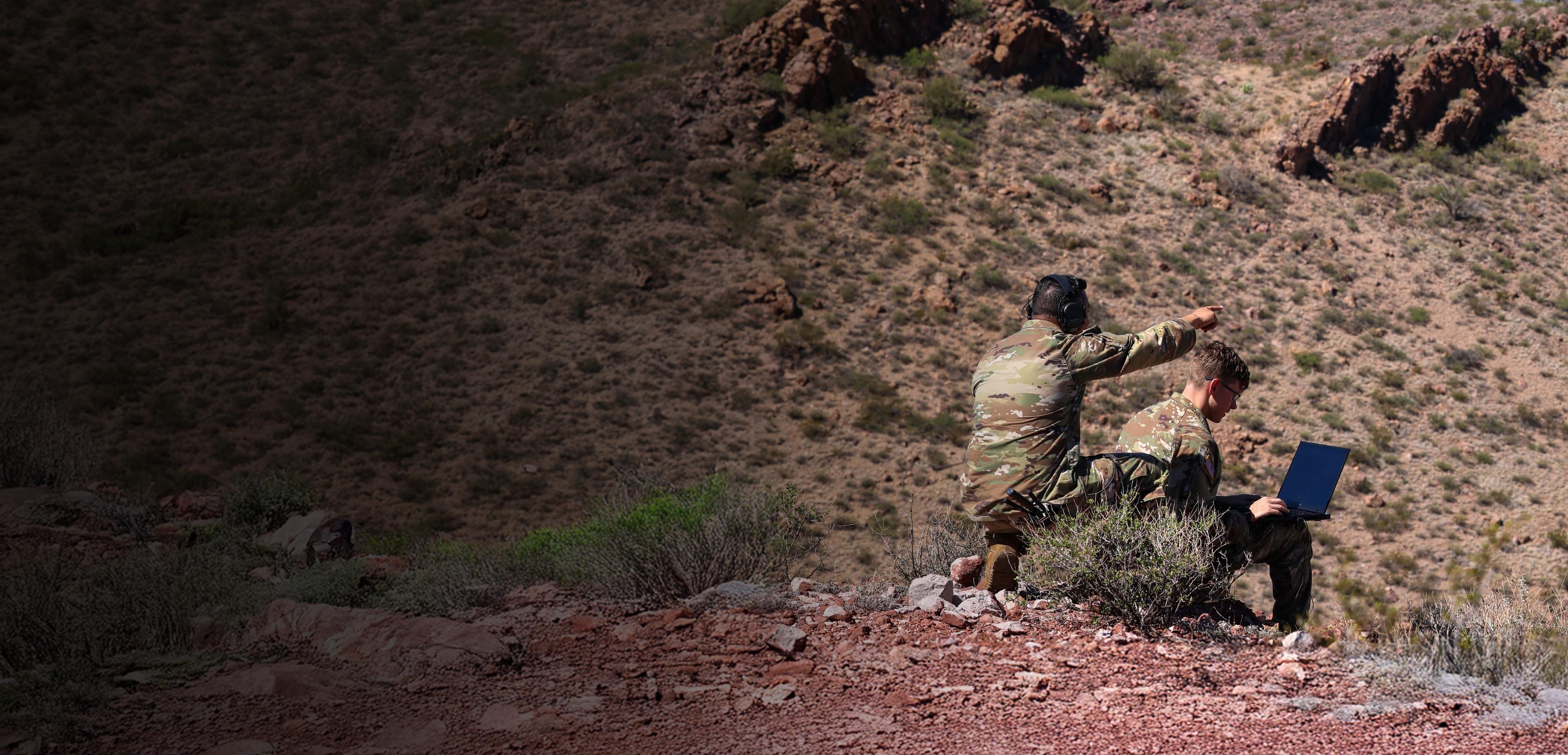 Two people sit on a grassy hillside, enjoying the view and each other's company under a clear blue sky.