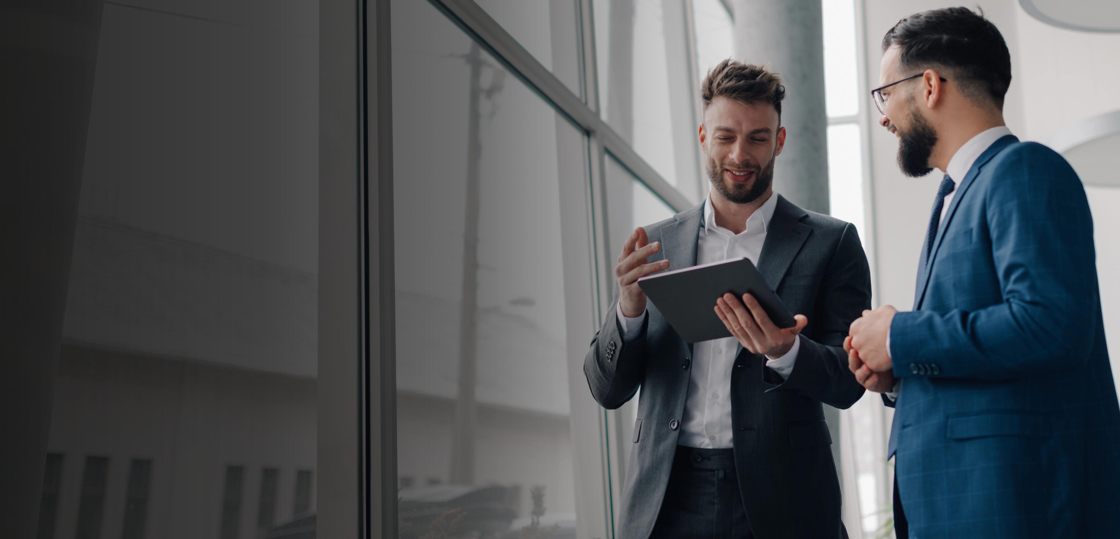 Two men in suits stand confidently in front of a modern building, engaged in conversation.