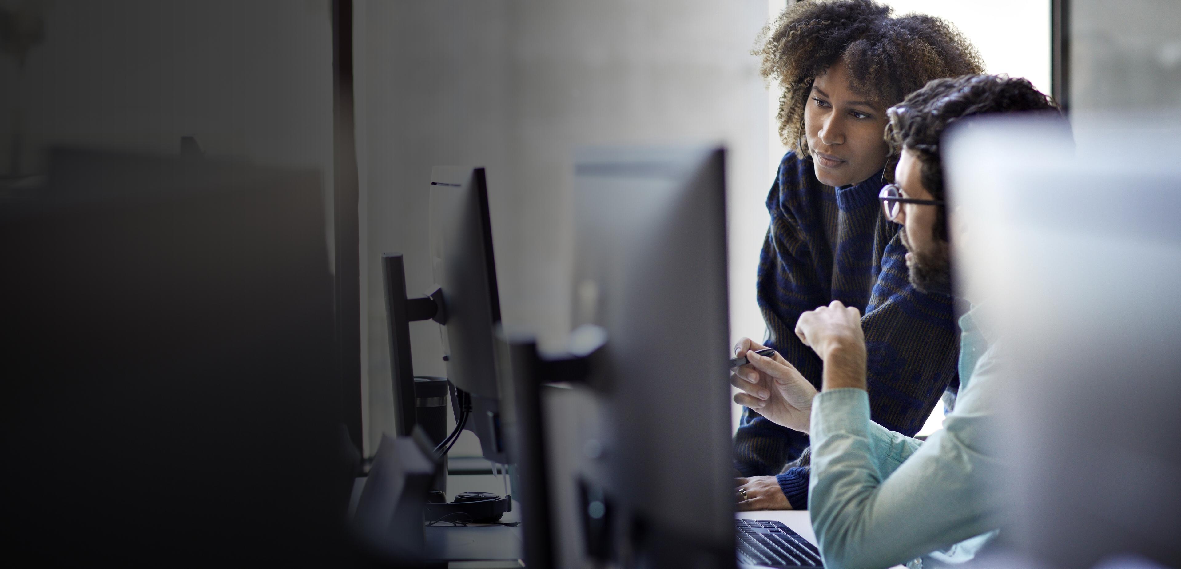 Two individuals focused on their computers while collaborating in a modern office environment.