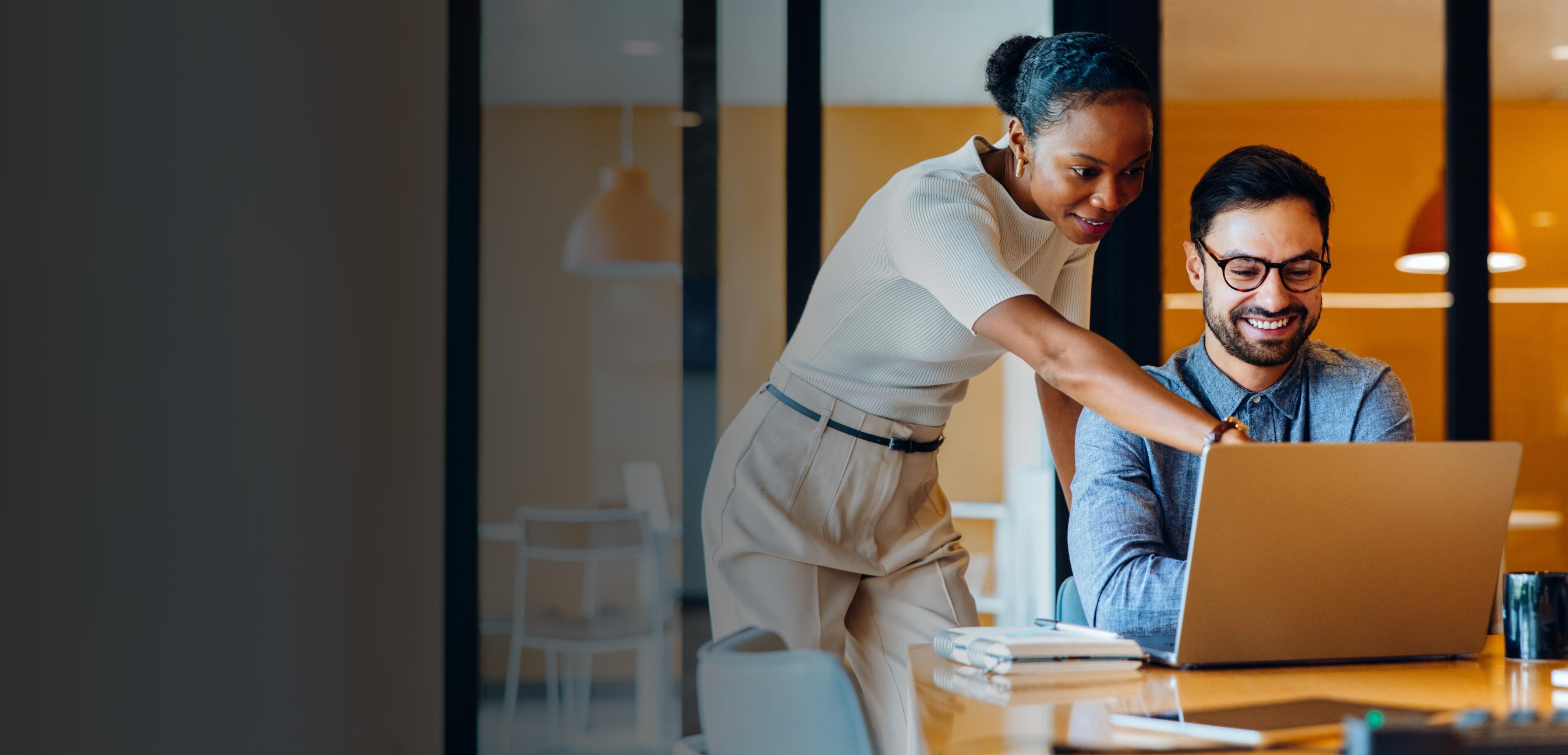 A man and woman collaborate on a laptop in a modern office setting, focused on their work.