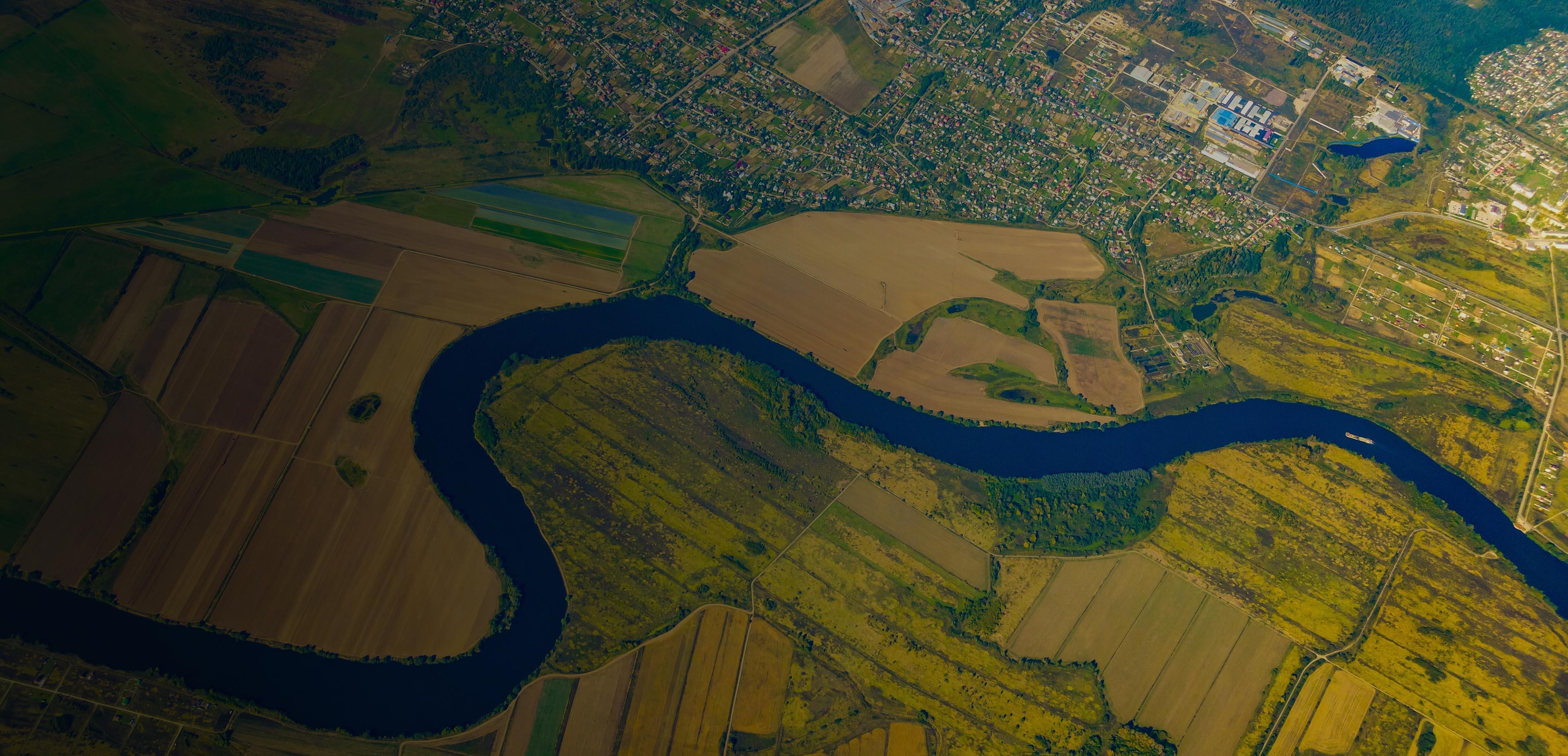 Aerial view showcasing a winding river surrounded by lush farmland and fields under a clear blue sky.