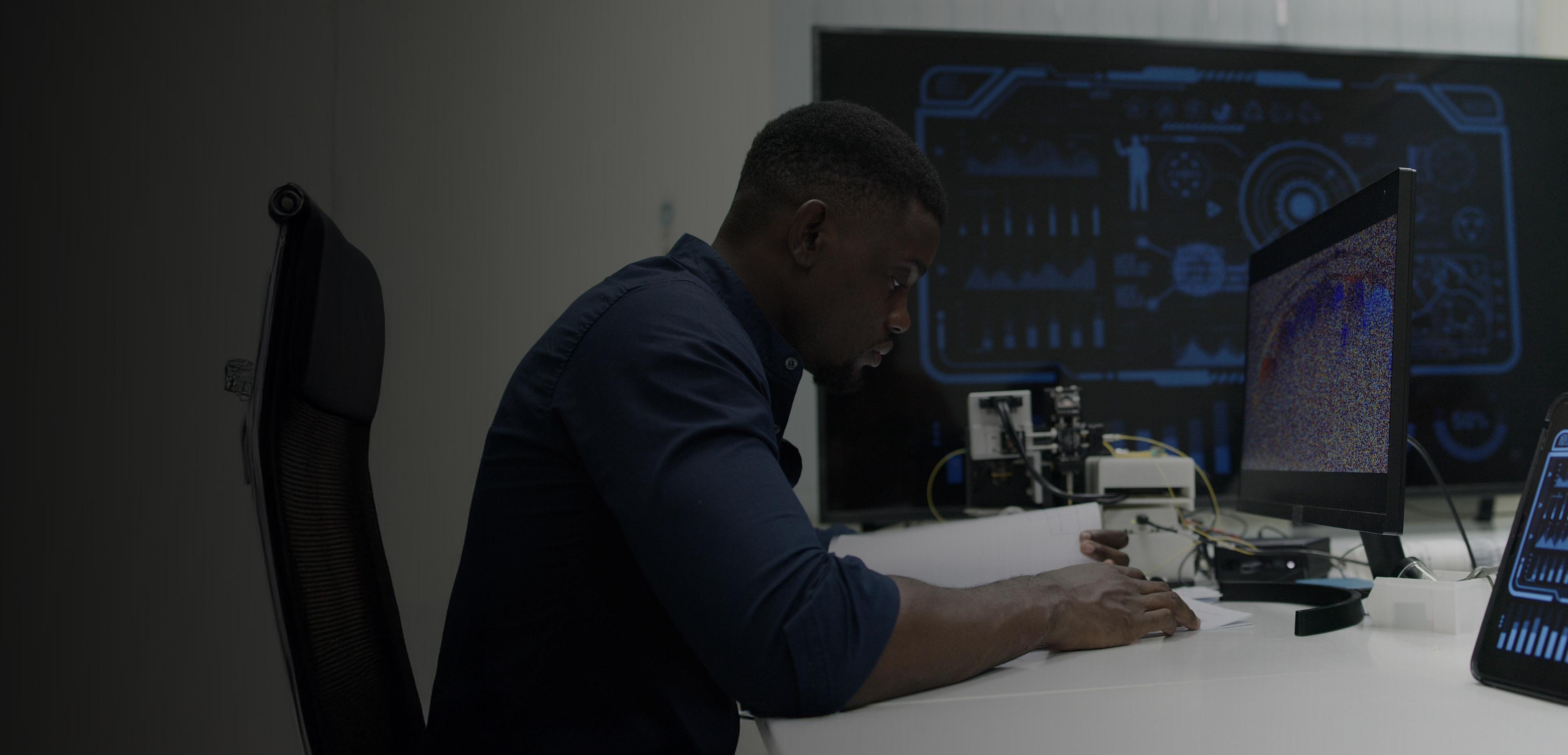 A man seated at a desk, working on a laptop with a monitor beside him.