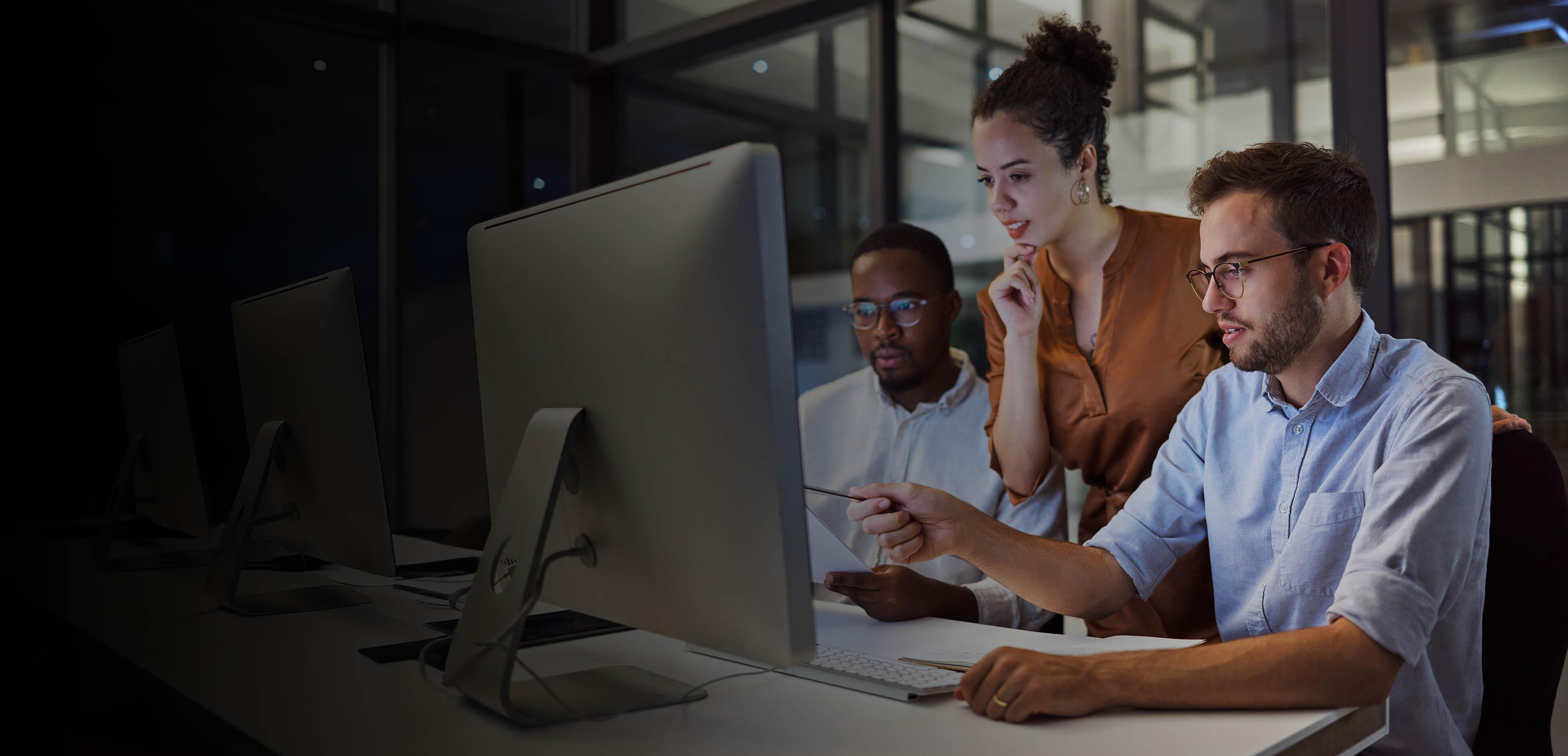 Three colleagues collaborating on a computer in a modern office setting.