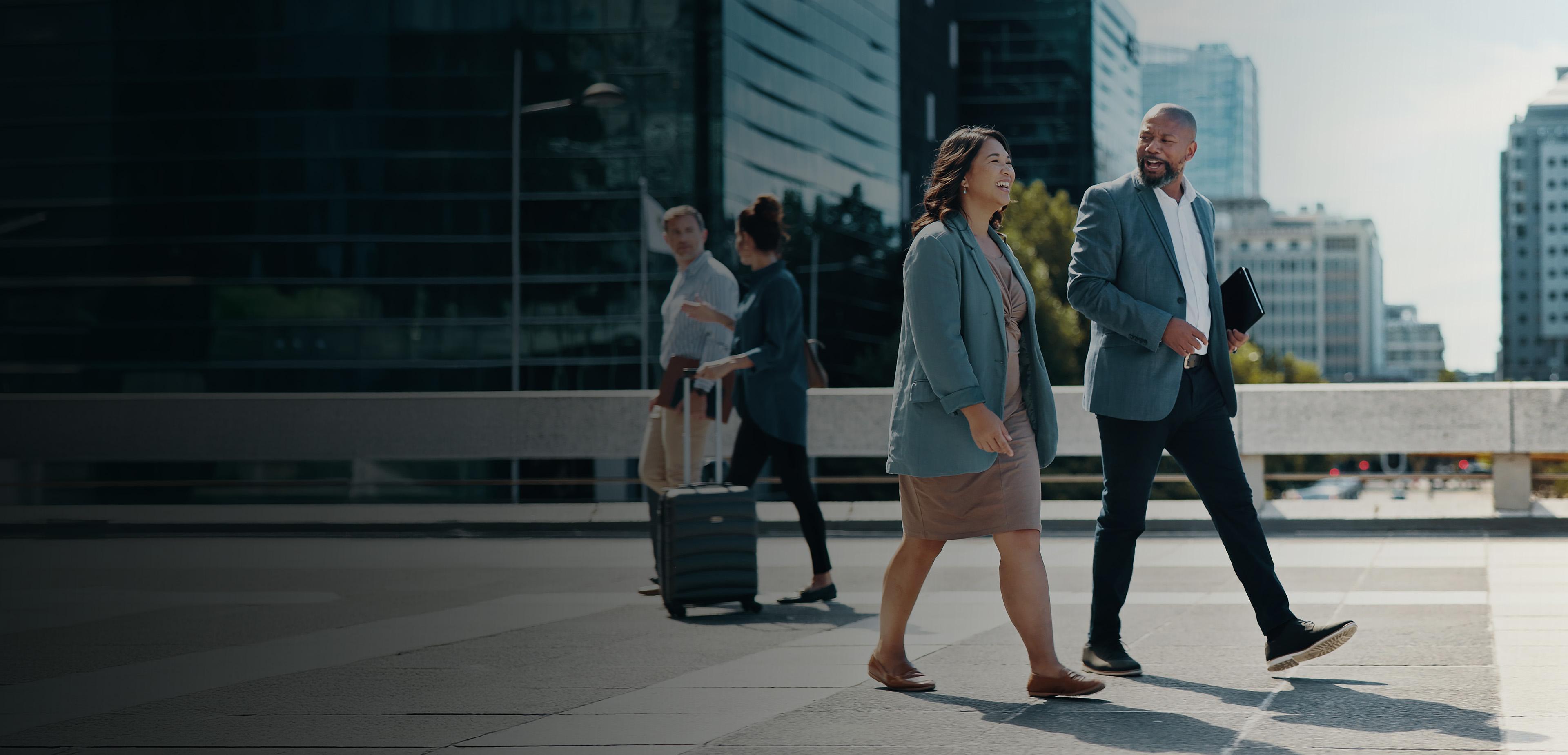Three business professionals walking together on a city street, engaged in conversation and dressed in formal attire.