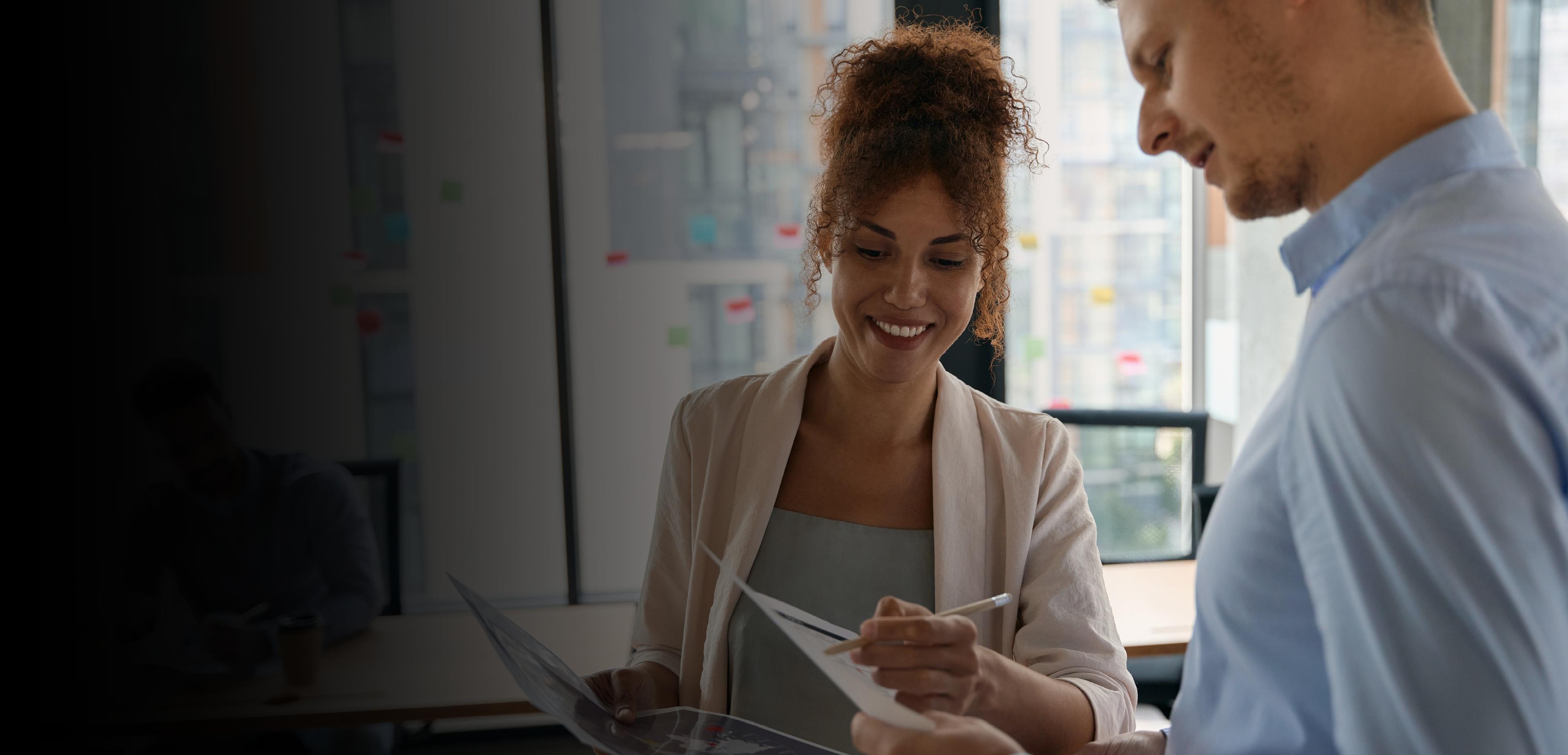 A man and woman review paperwork together in a modern office setting.