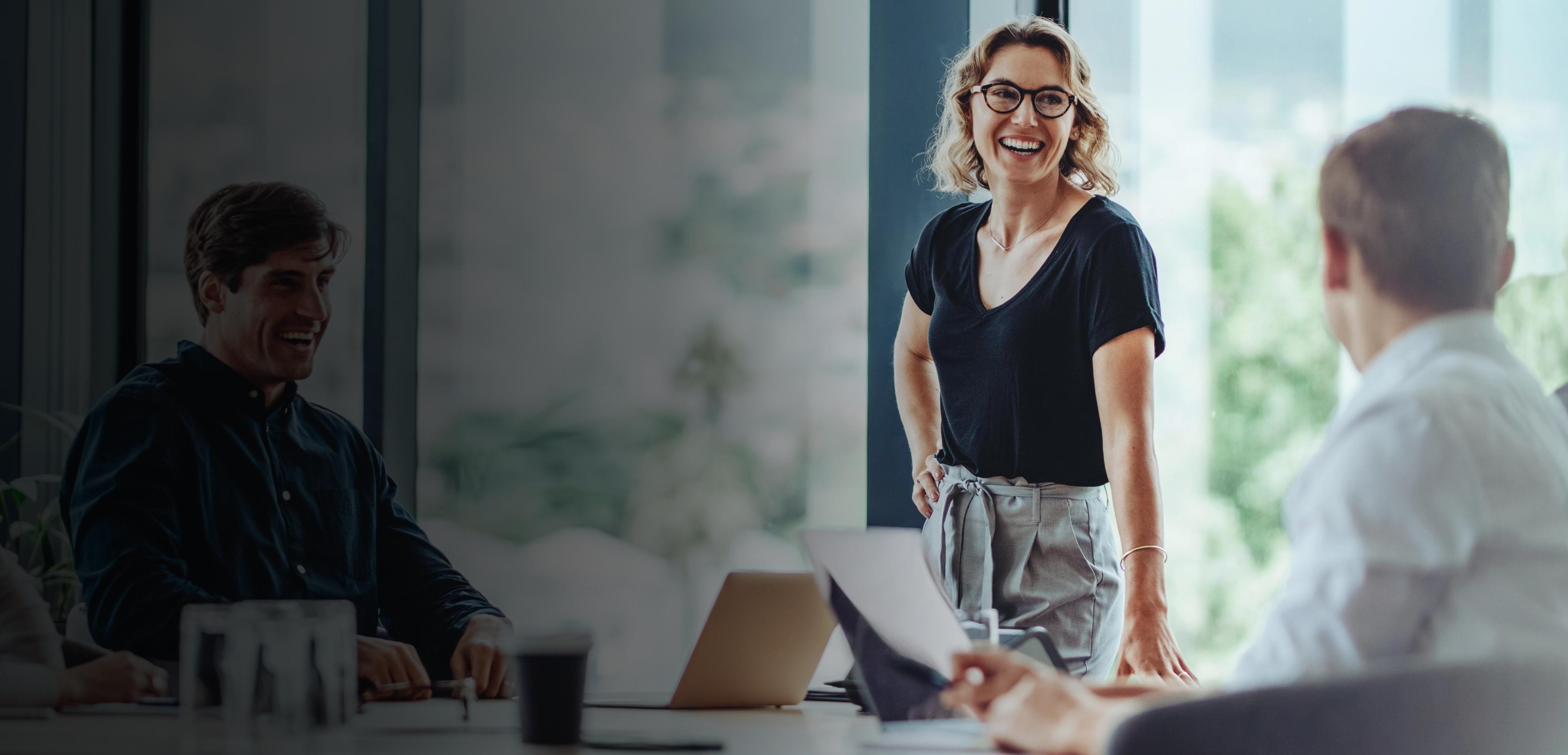 A woman speaks to a man in a meeting room, engaged in a professional discussion.