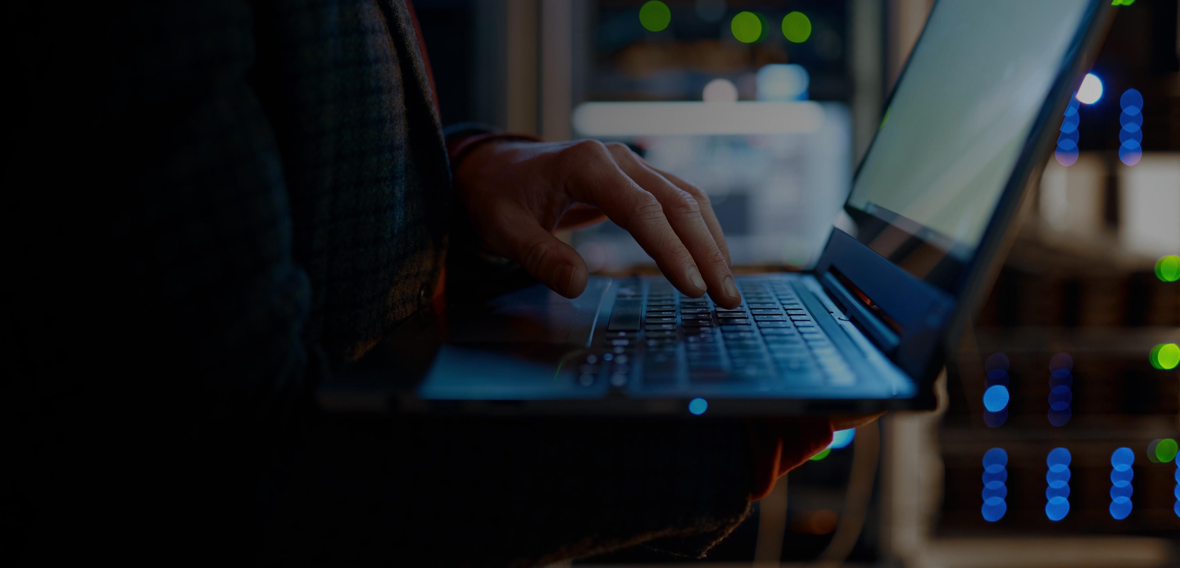 A person focused on typing on a laptop computer, with hands positioned on the keyboard and a screen illuminated.