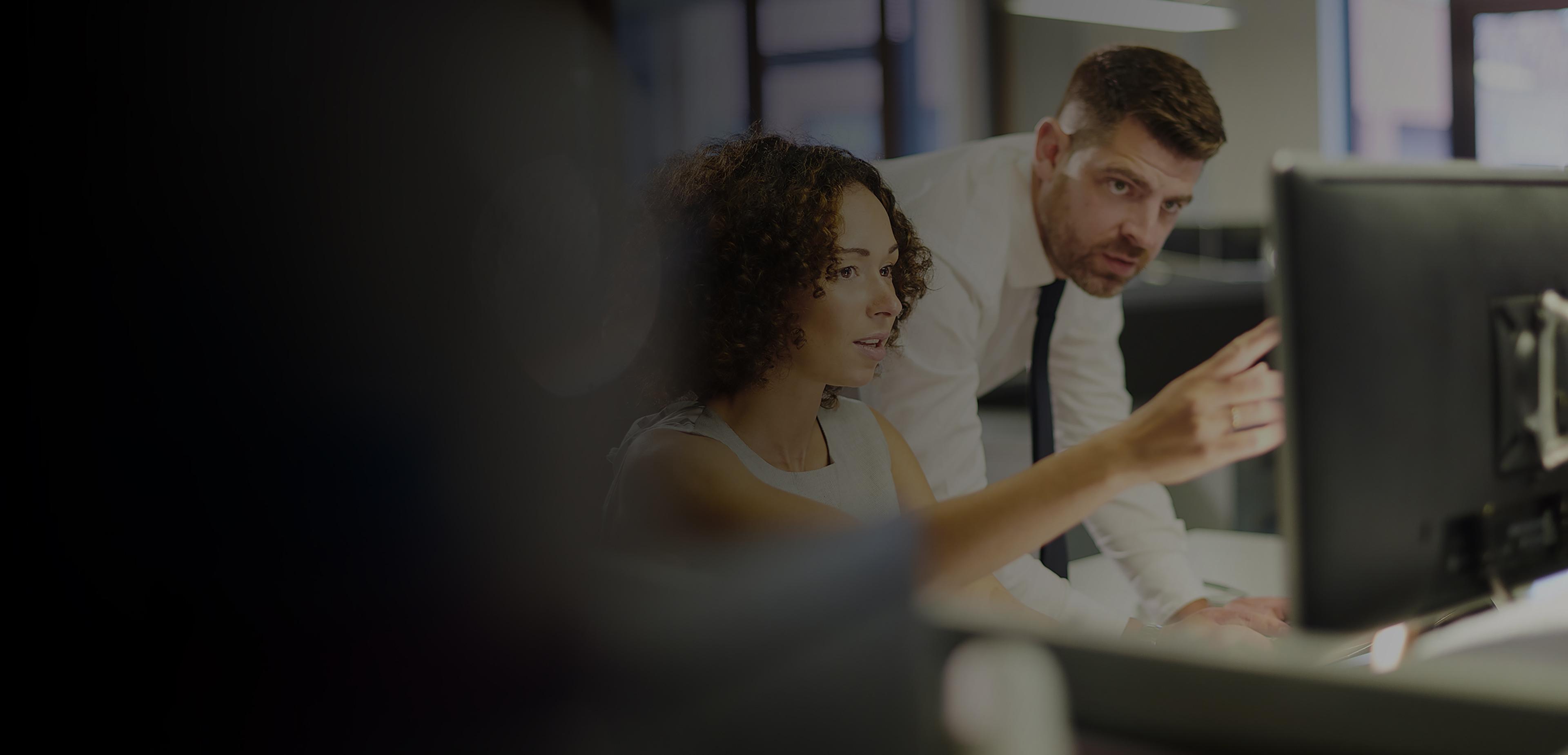 A man and woman collaborate on a computer in a modern office setting, focused on their work and sharing ideas.