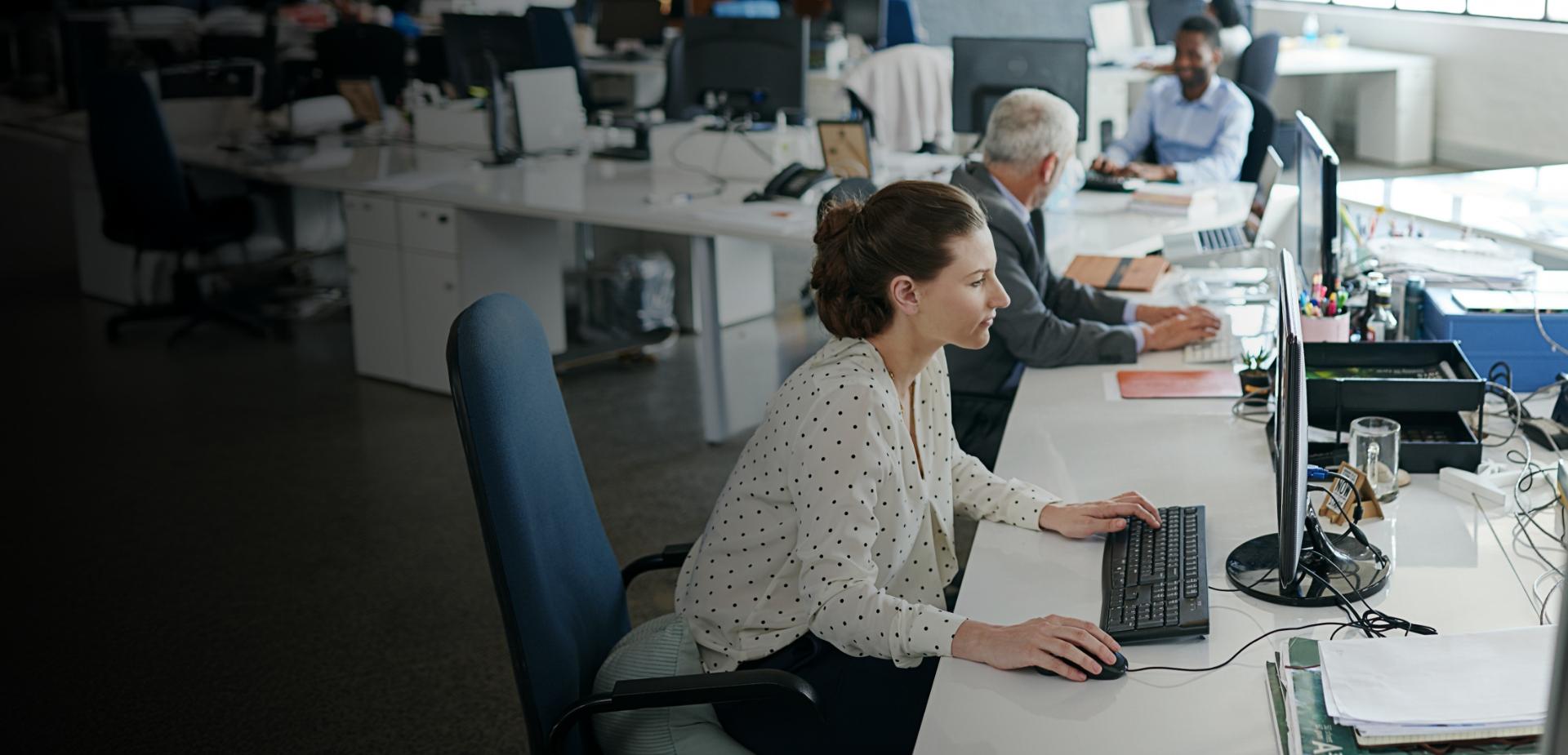 A woman focused on her computer while working in a modern office environment.