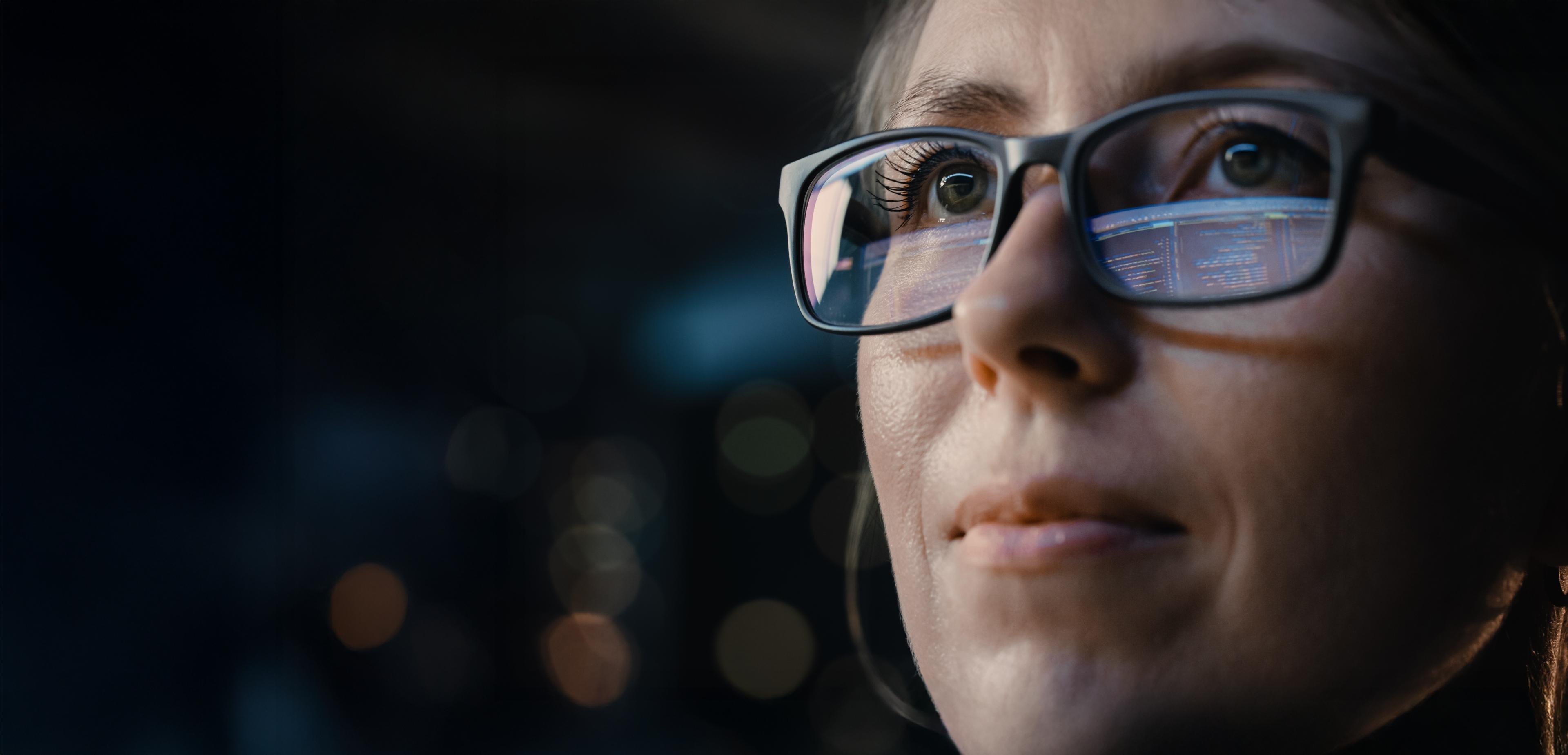 A woman with glasses gazes thoughtfully to the side, her expression contemplative and focused.