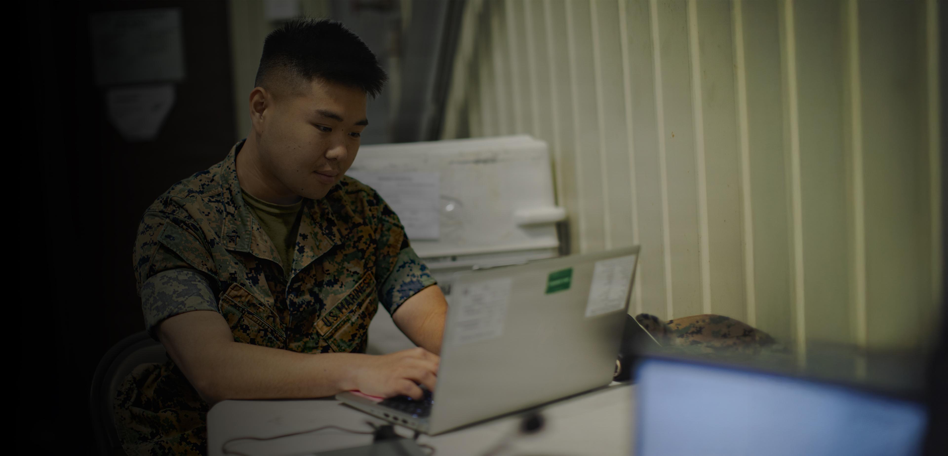 A man in military uniform seated at a desk, focused on paperwork in a professional office setting.