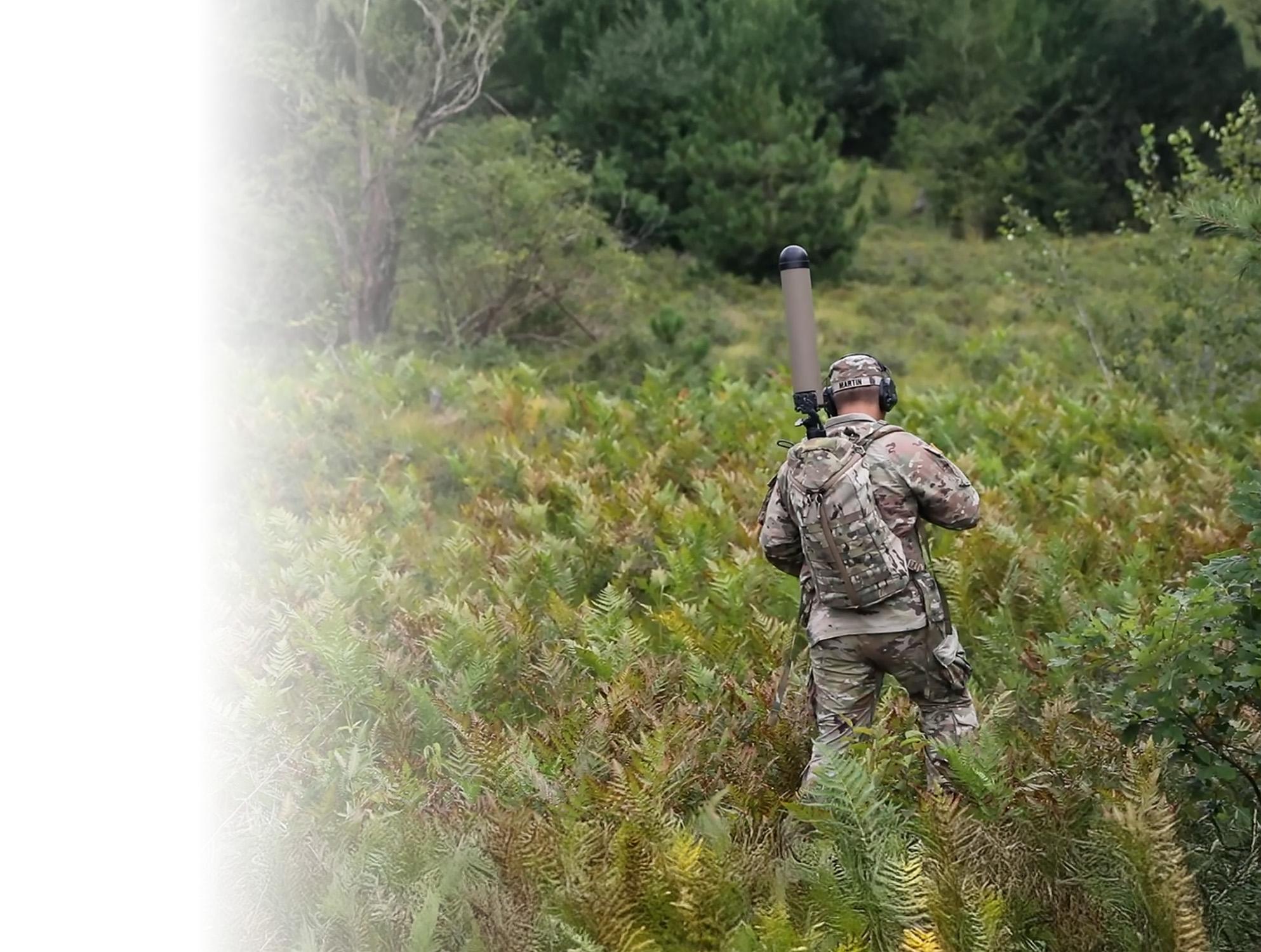 A man carrying a backpack walks through a field of tall grass, surrounded by nature's greenery.
