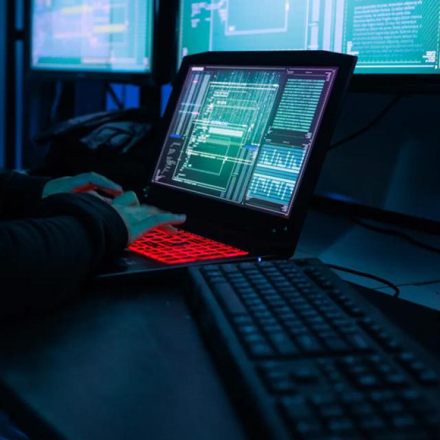 A dark lit room with a person typing on a red lit keyboard.