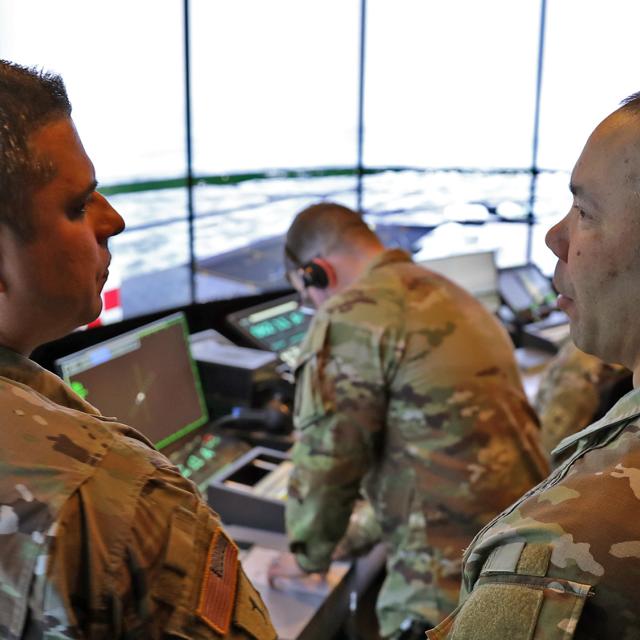 Two army soldiers examining a computer screen inside of a command and control center.