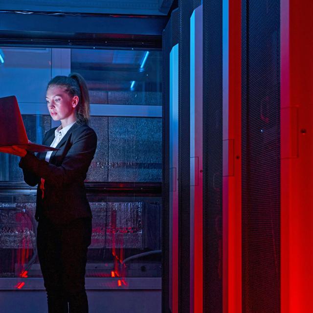 A woman is positioned in a server room as she monitors the complex array of servers and equipment.