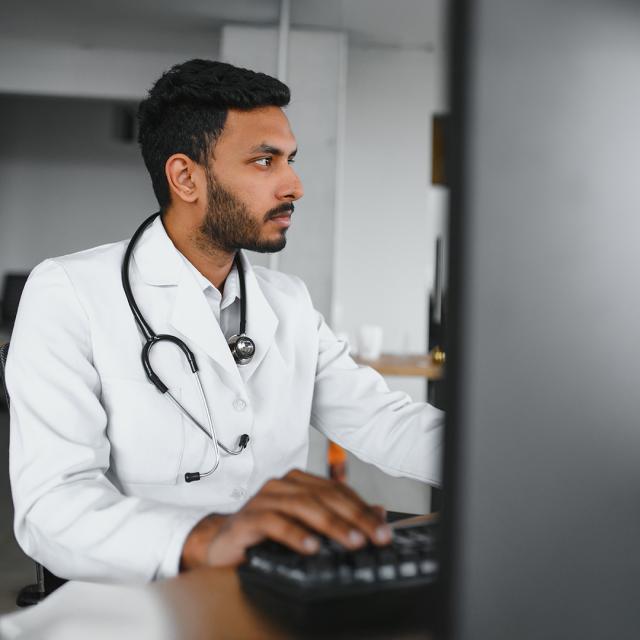 A doctor working on a computer in a medical facility setting.