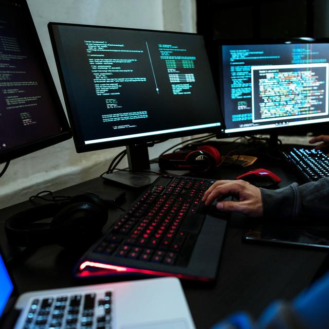 A person seated at a desk, focused on three computer screens displaying various tasks and information.