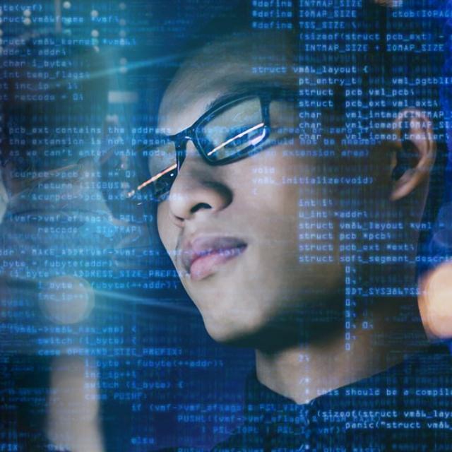 A man wearing glasses, focused on a computer screen, engaged in work or study.