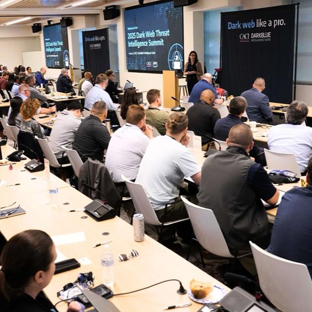 A large group of people seated at tables in a conference room, engaged in discussion and collaboration.