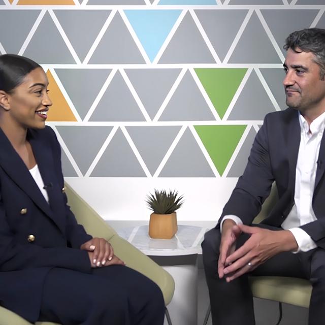 A man and woman engaged in conversation while seated in chairs, sharing ideas in a relaxed setting.
